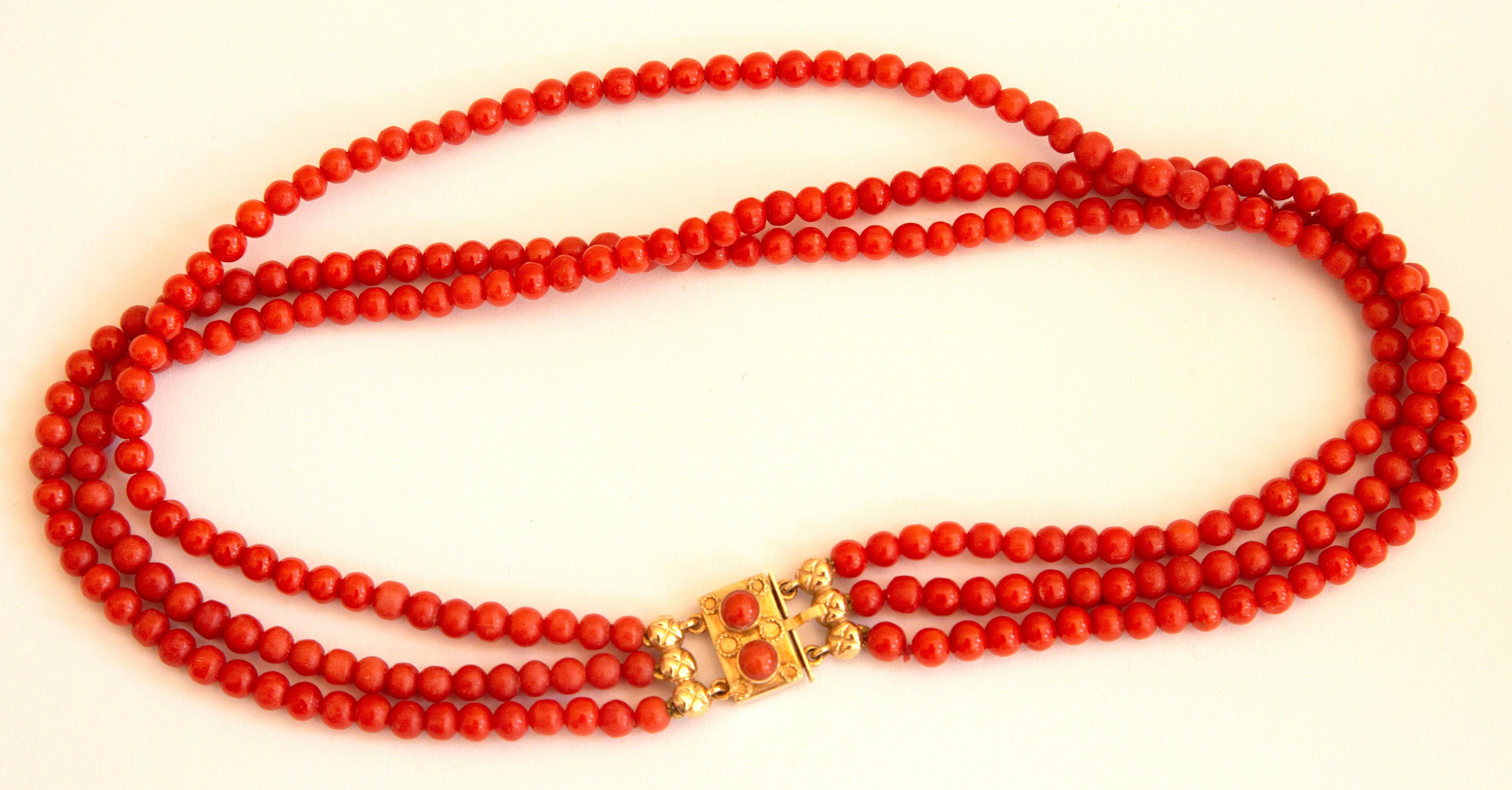 An antique necklace made of natural red coral beads with 14 karat golden clasp. The bracelet features three strands of round - shaped beads. The diameter of the beads is ca. 5 mm and the color is red. The clasp features a rectangular shape with two