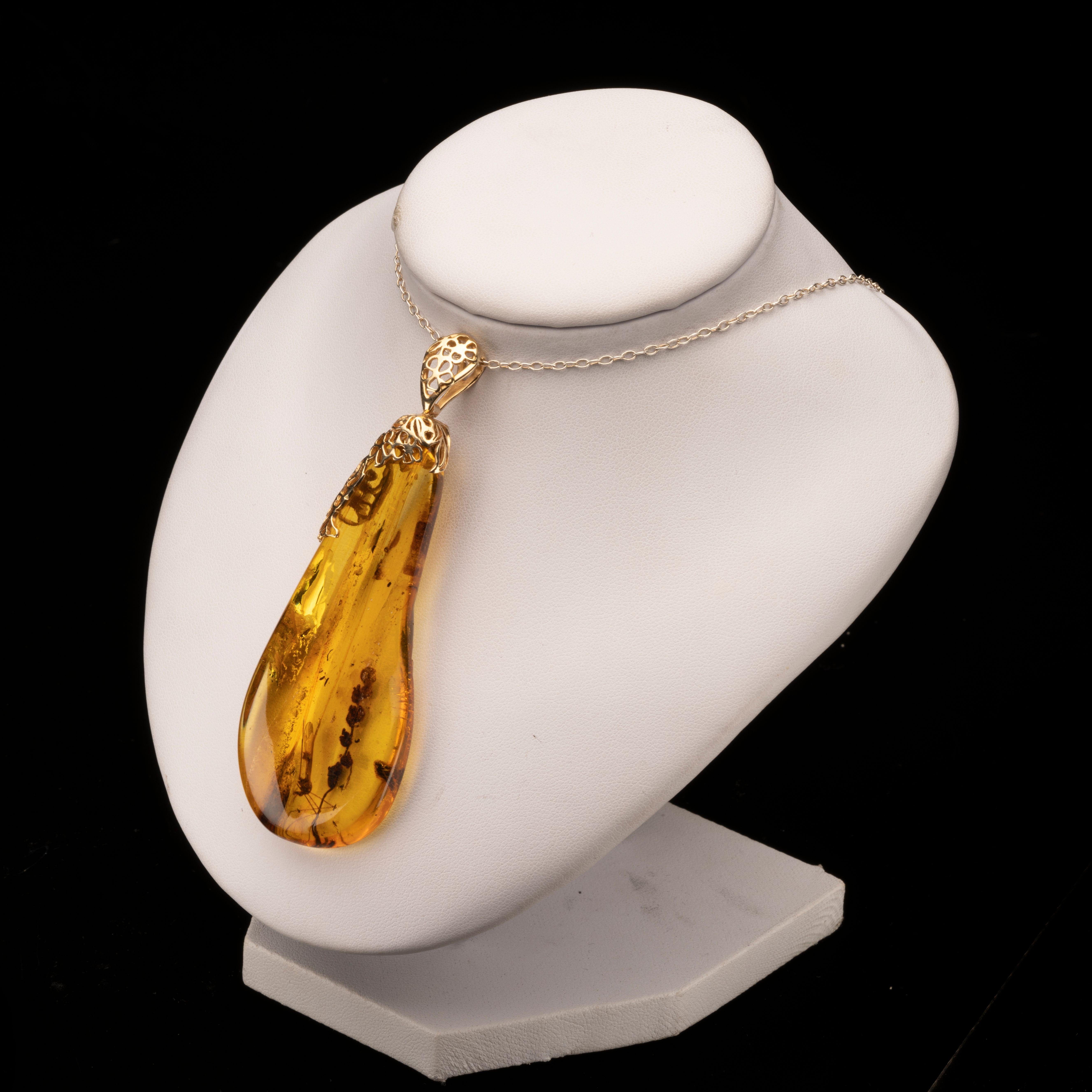 This piece of Baltic amber features incredible color and clarity and boasts preserved plants and insects including at least one completely visible mosquito. Polished to a handsome luster, the specimen has been made into a pendant with an intricately