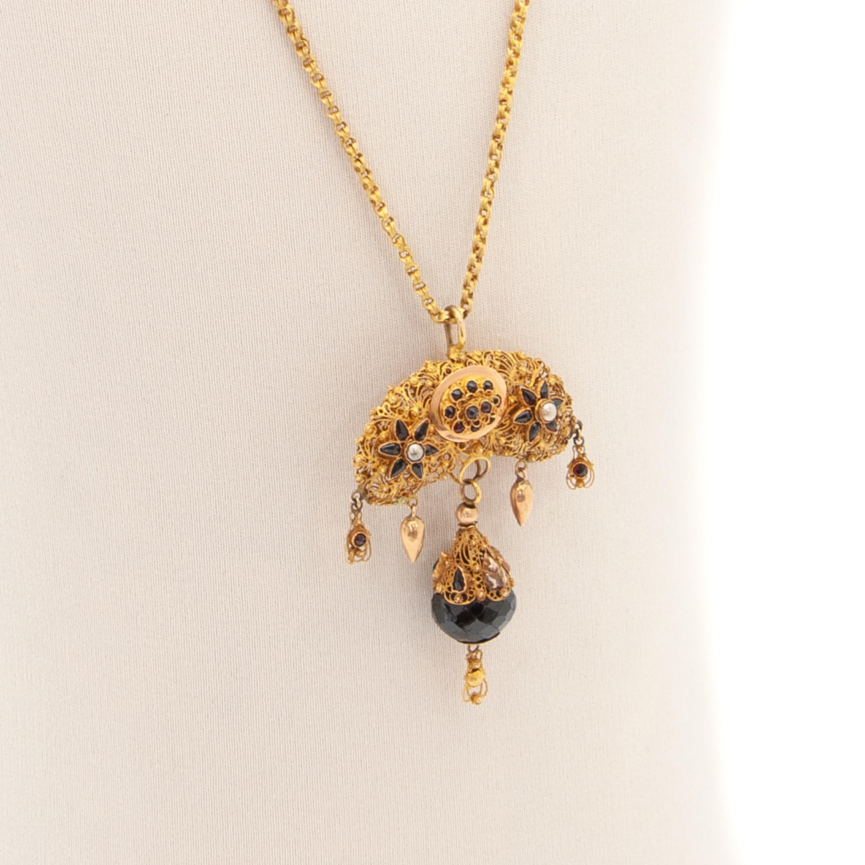 A beautiful antique pendant necklace of the late 19th century and handmade in the Netherlands. The pendant is created in 14 karat yellow gold and made of fine filigree and cannetille work set with garnets and seed pearls. The craftsmanship of this