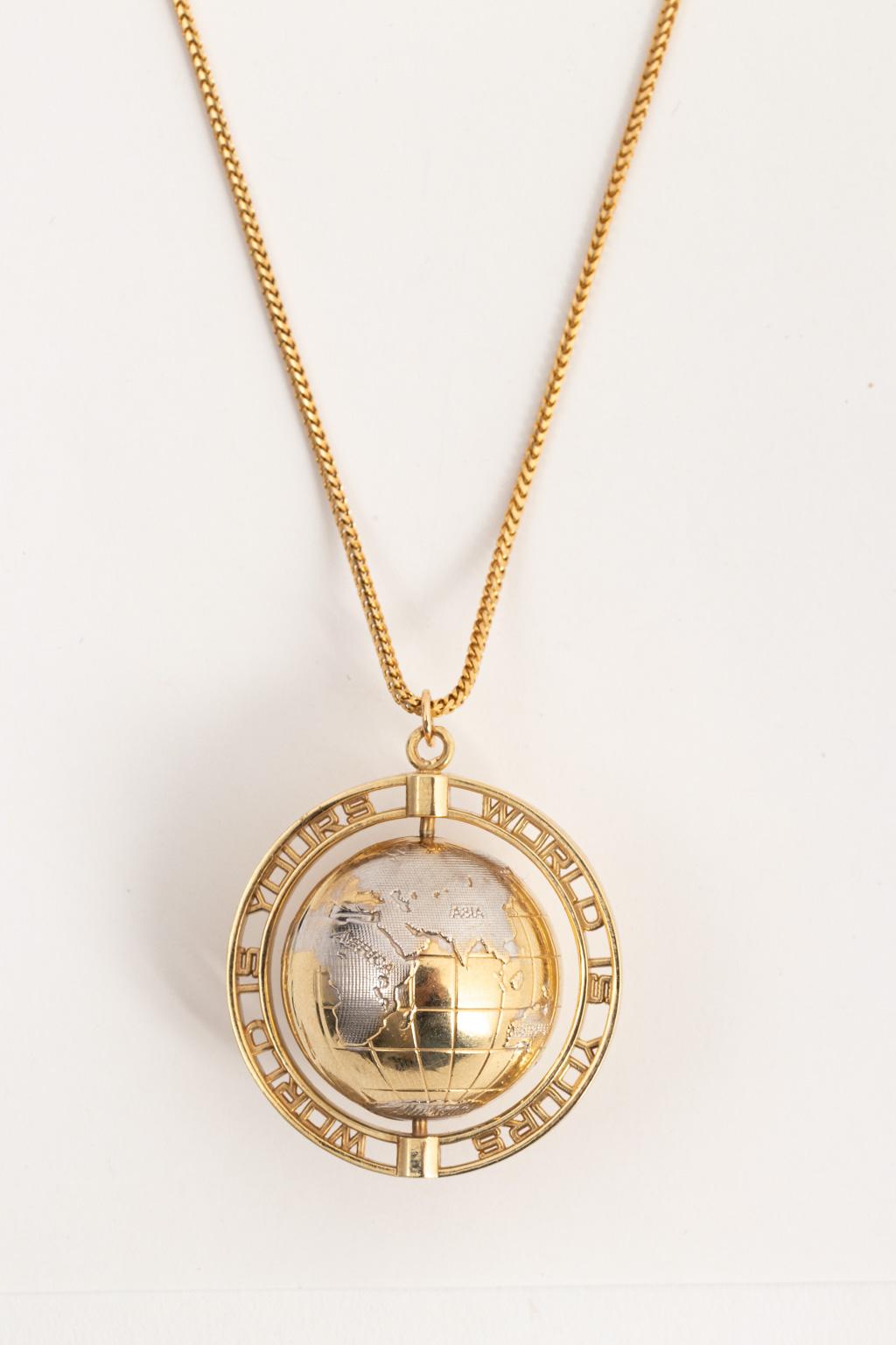 Circa 1950-1960s Mid-Century Modern style 14 karat yellow and white gold globe charm on a 14 karat yellow gold 24.00 Inch herringbone design chain. The globe charm swivels in between an open circular support for the charm and also serves as a design