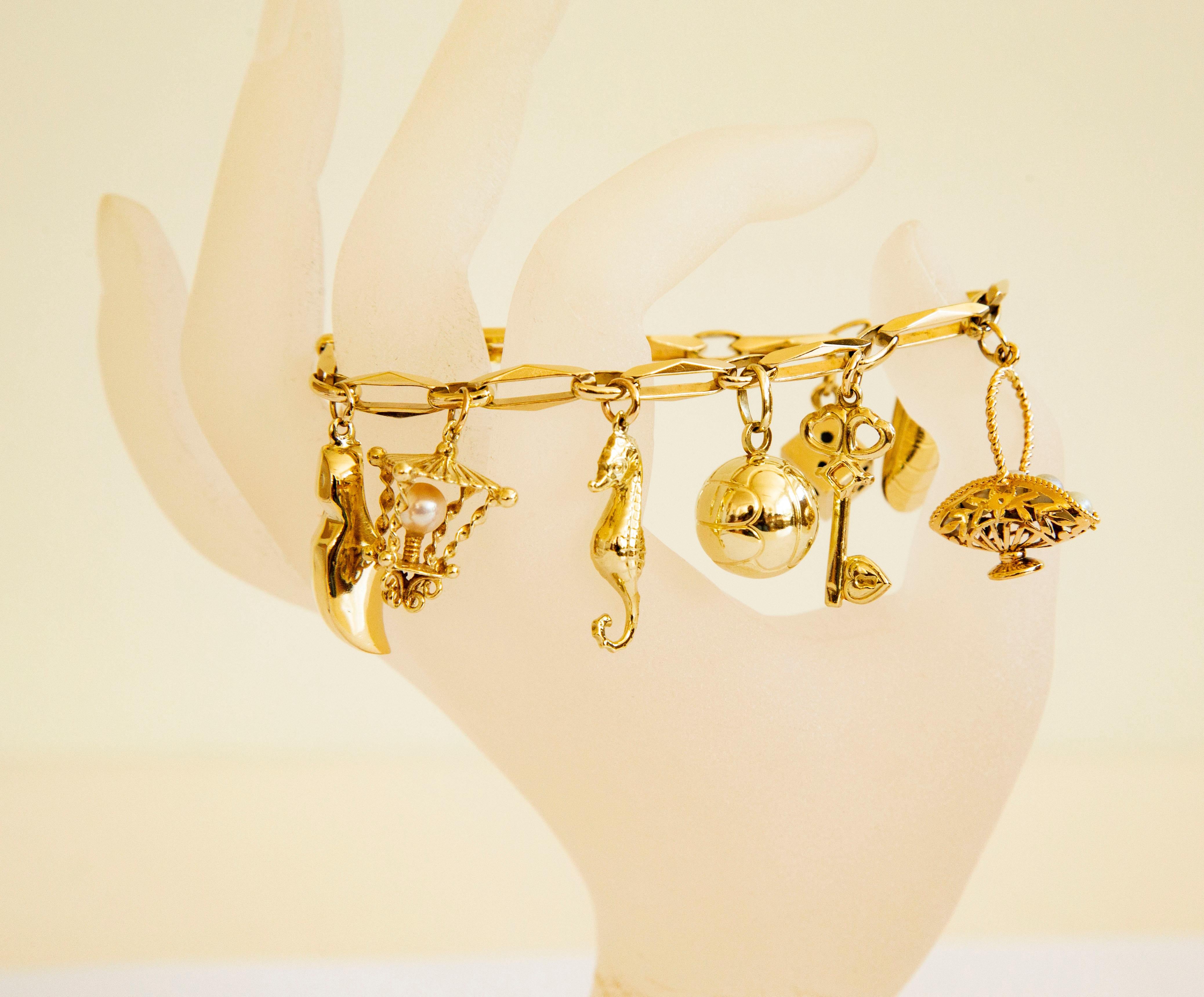 A vintage 14 karat yellow gold bracelet with 10 charms, including a hunting horn, a heart, a clog, a lantern, a seahorse, a ball, a key, a basket with five pearls, a mussel, and a dice. 
The bracelet was manufactured in the middle of the 20th