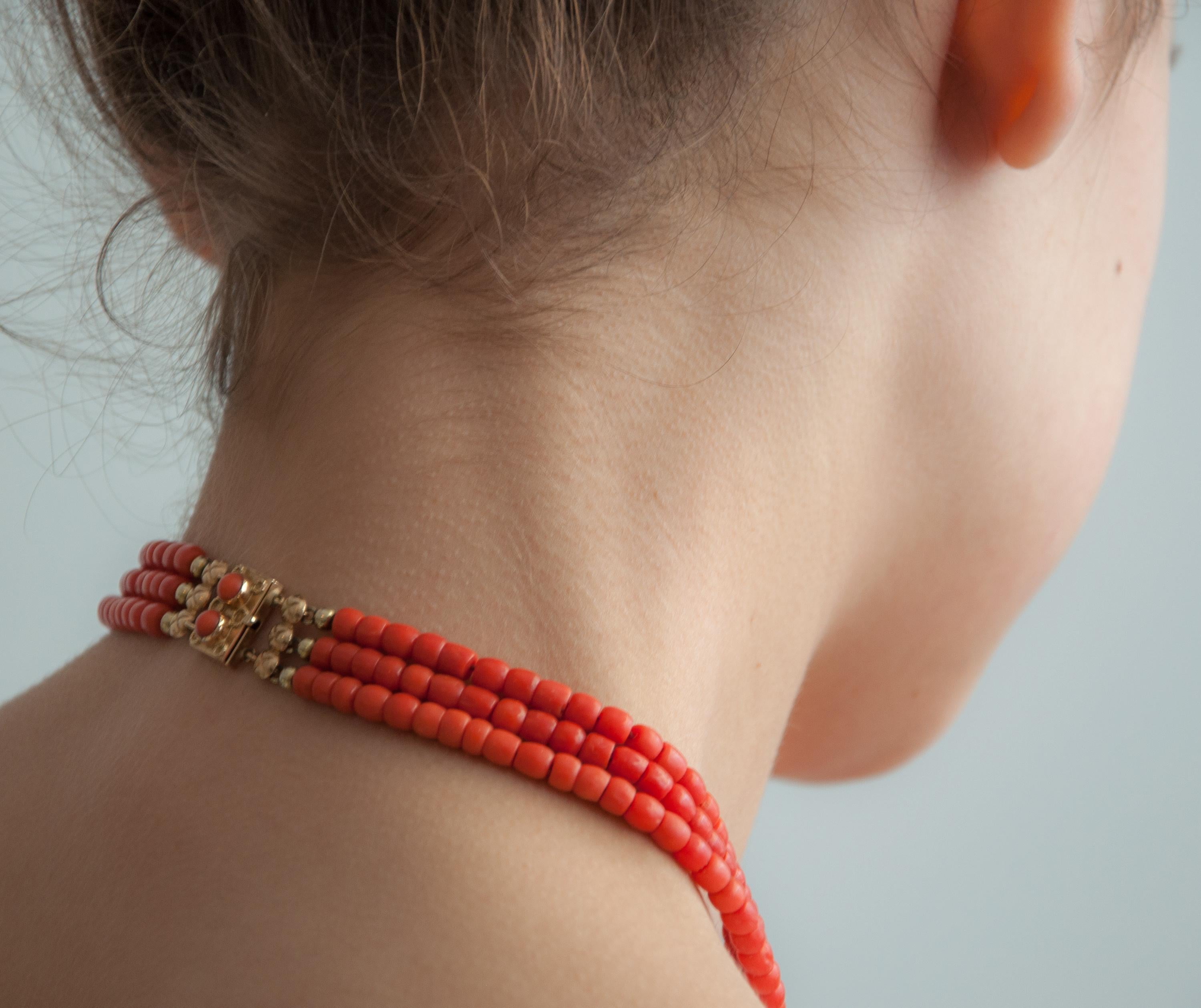 This vintage natural red coral beaded necklace is set with a 14 karat gold clasp. This three-strand coral necklace is strung with barrel-shaped beads, which are smooth and measure equal in size. The beautiful clasp has a rectangular shape with two