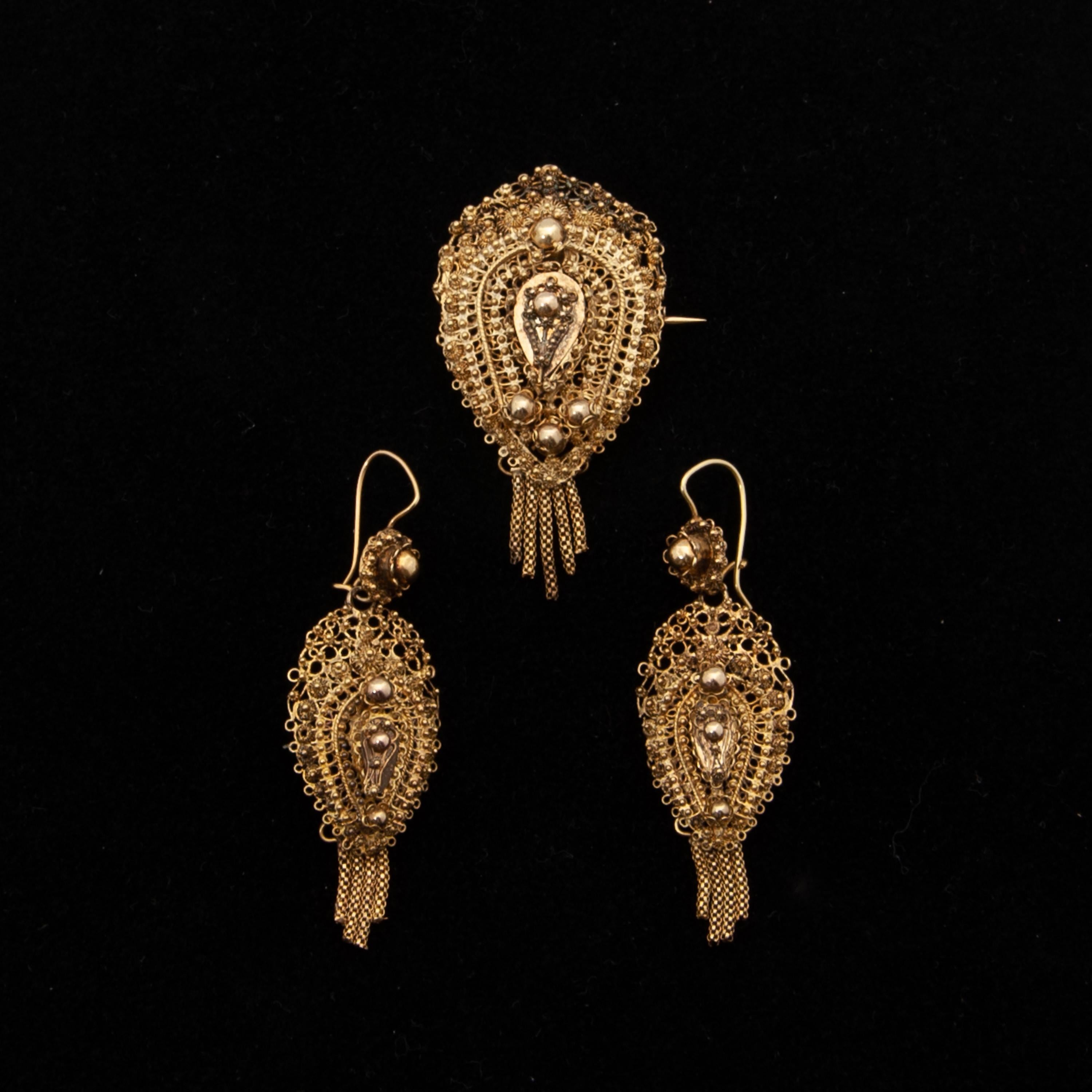 This beautiful antique jewelry set is consisting of a pair of earrings and a brooch. The set has a beautiful filigree and cannetille work design. Both, earrings and brooch, have dangling tassels below the top. These remarkable pieces of jewelry were