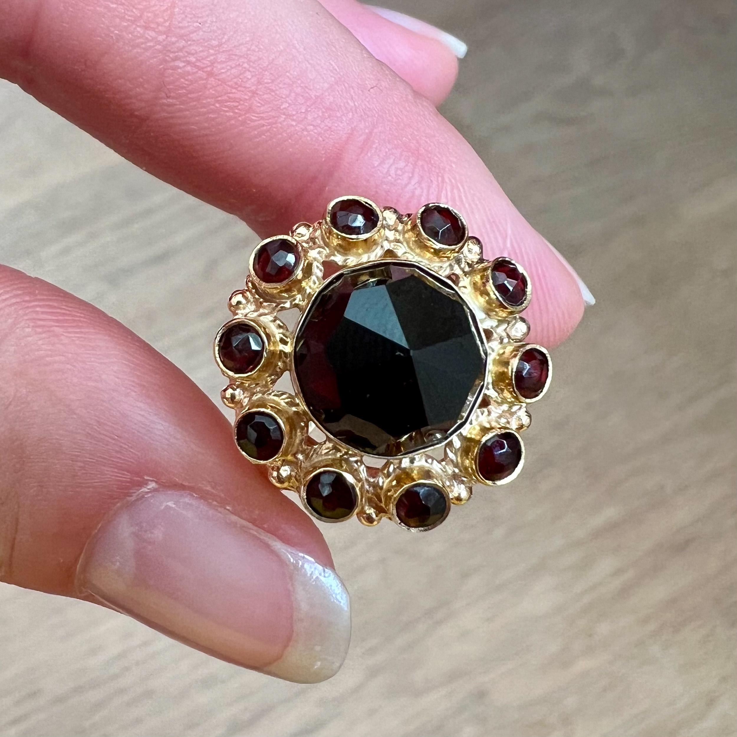 A vintage garnet cluster ring set in a 14 karat gold mounting. This gorgeous ring features a large round faceted garnet surrounded by ten smaller faceted garnets. The stones are bezel set and between the garnet stones the frame has an openwork