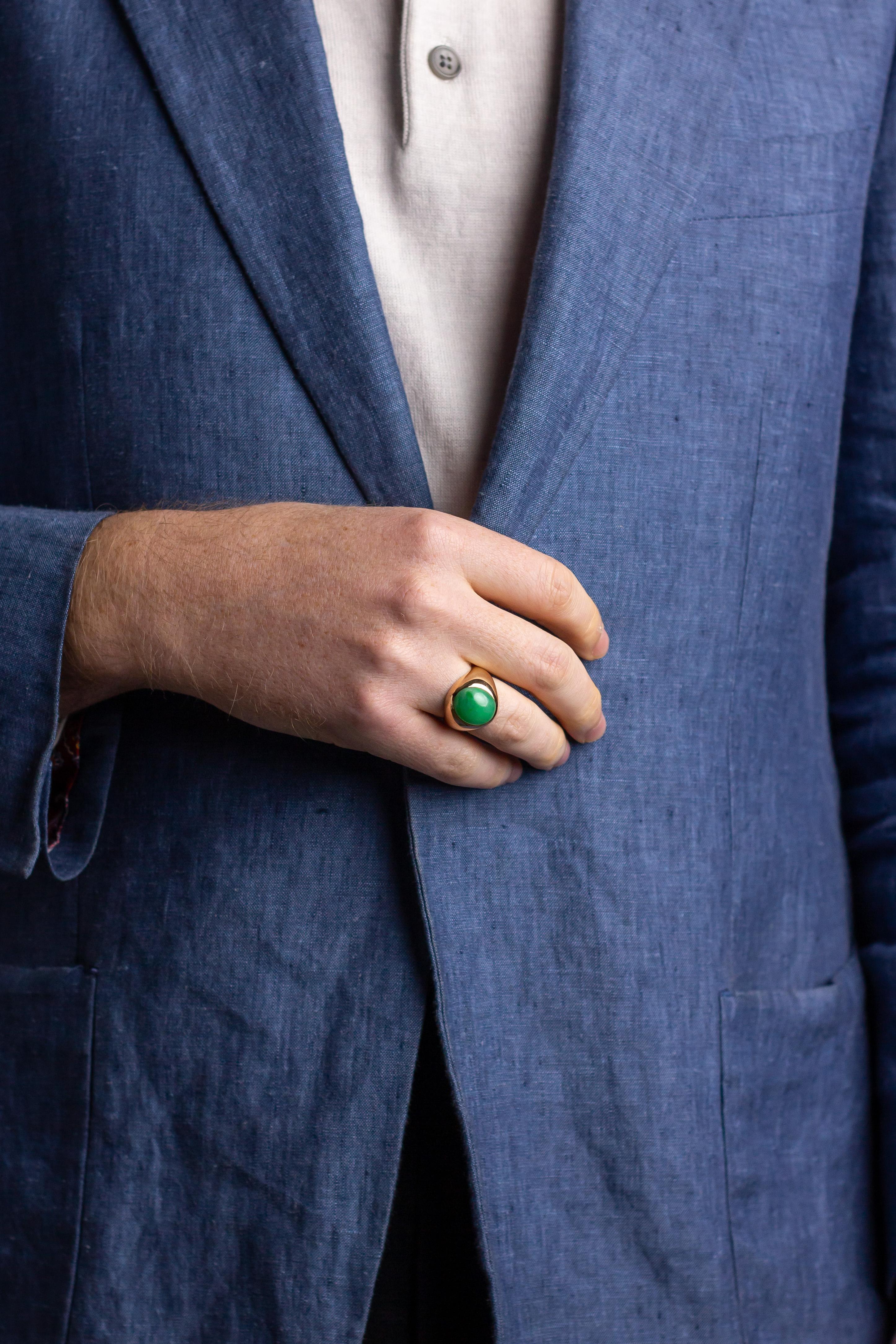 This sleek and simple jadeite jade ring is crafted from 14 karat yellow gold. The centre of the ring features a rub-over set piece of oval cabochon cut mottled green jadeite jade. The simple gold ring features a tapered shank with thickened gold