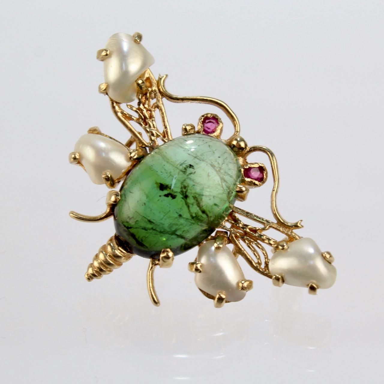 A very fine figural 14k gold bee (or insect) brooch with wings that move.

Prong-set with a green tourmaline oval cabochon at the center of the body of the bee. 

Four pearls are set at the ends of the bee's wings. The two bottom wings are hinged.