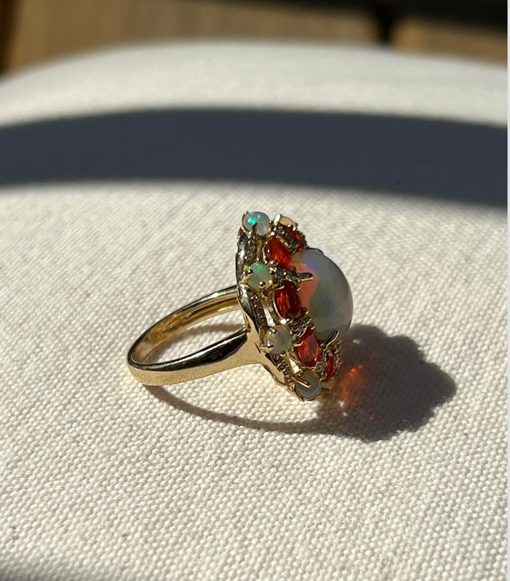 One 14 karat yellow gold ring set with one 12x10 oval Ethiopian opal, eight 3.10x3.10mm opals, (8) eight (8) Mexican fire opals, and forty-four (44) brilliant cut diamonds, approximately 0.15 carat total weight with matching G/H color and VS/SI1