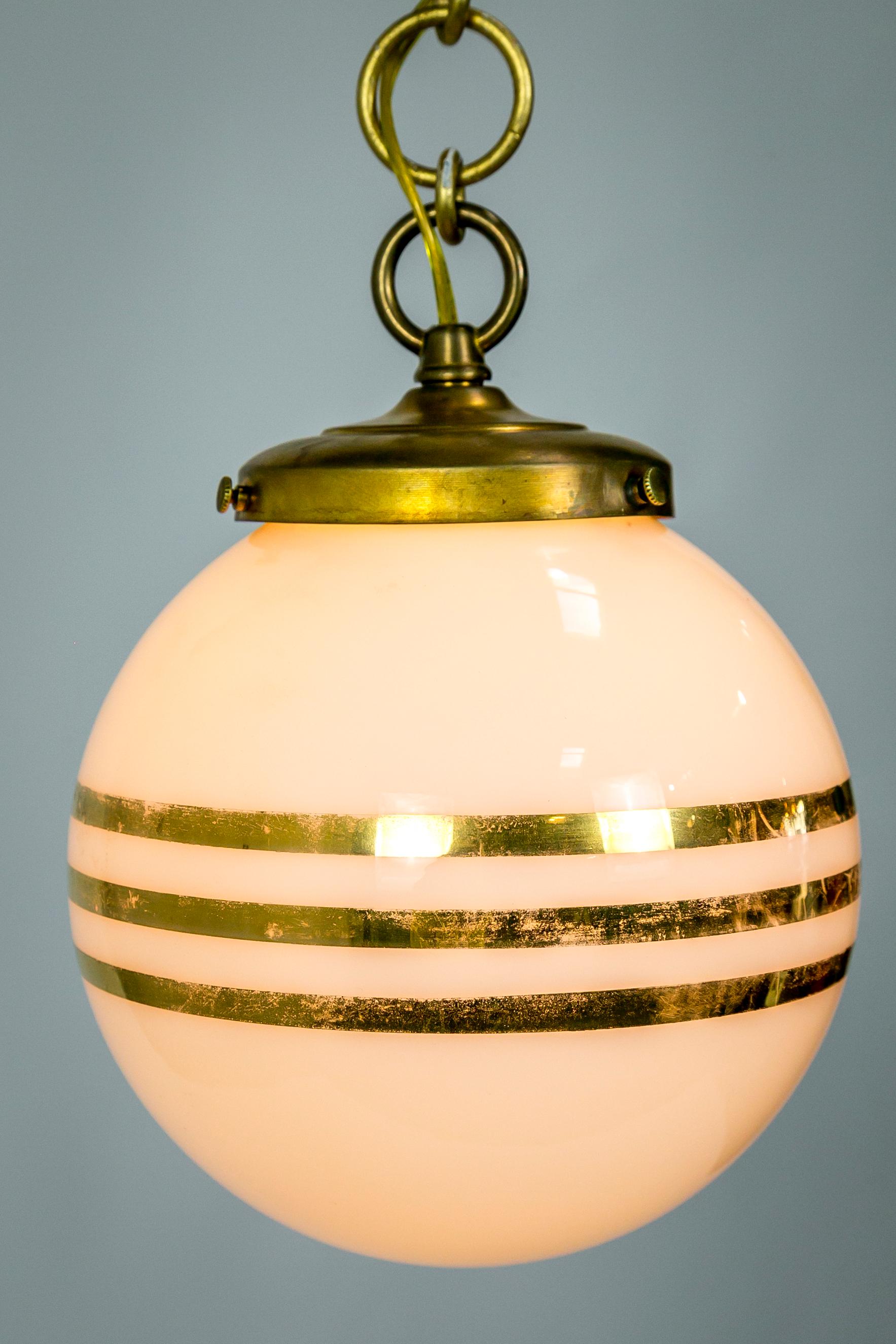 This pair of 1960s American white glass globes with 14-carat gold stripes have been newly made into pendants; with and gold finished canopy and decorative chain with circular links. Measures: 48” total drop; 7.5” diameter x 10.5” height.