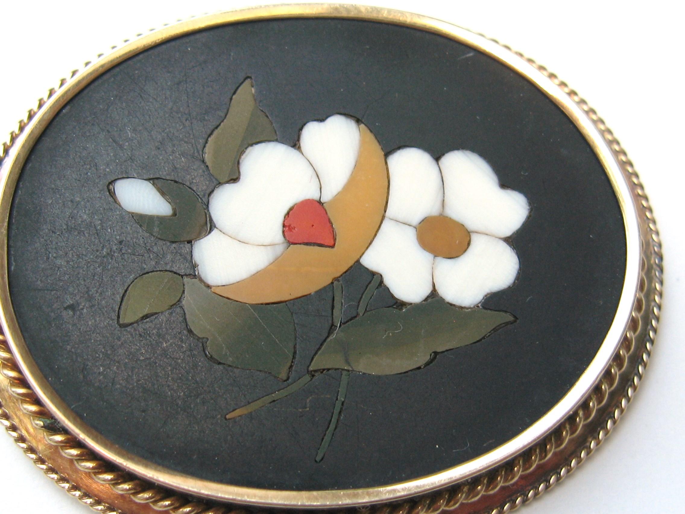 A wonderful antique Victorian Circa 1890s Italian Pietra Dura Floral Mourning Brooch featuring a mosaic floral inlay set in 14k gold / onyx. Measuring 1.86
