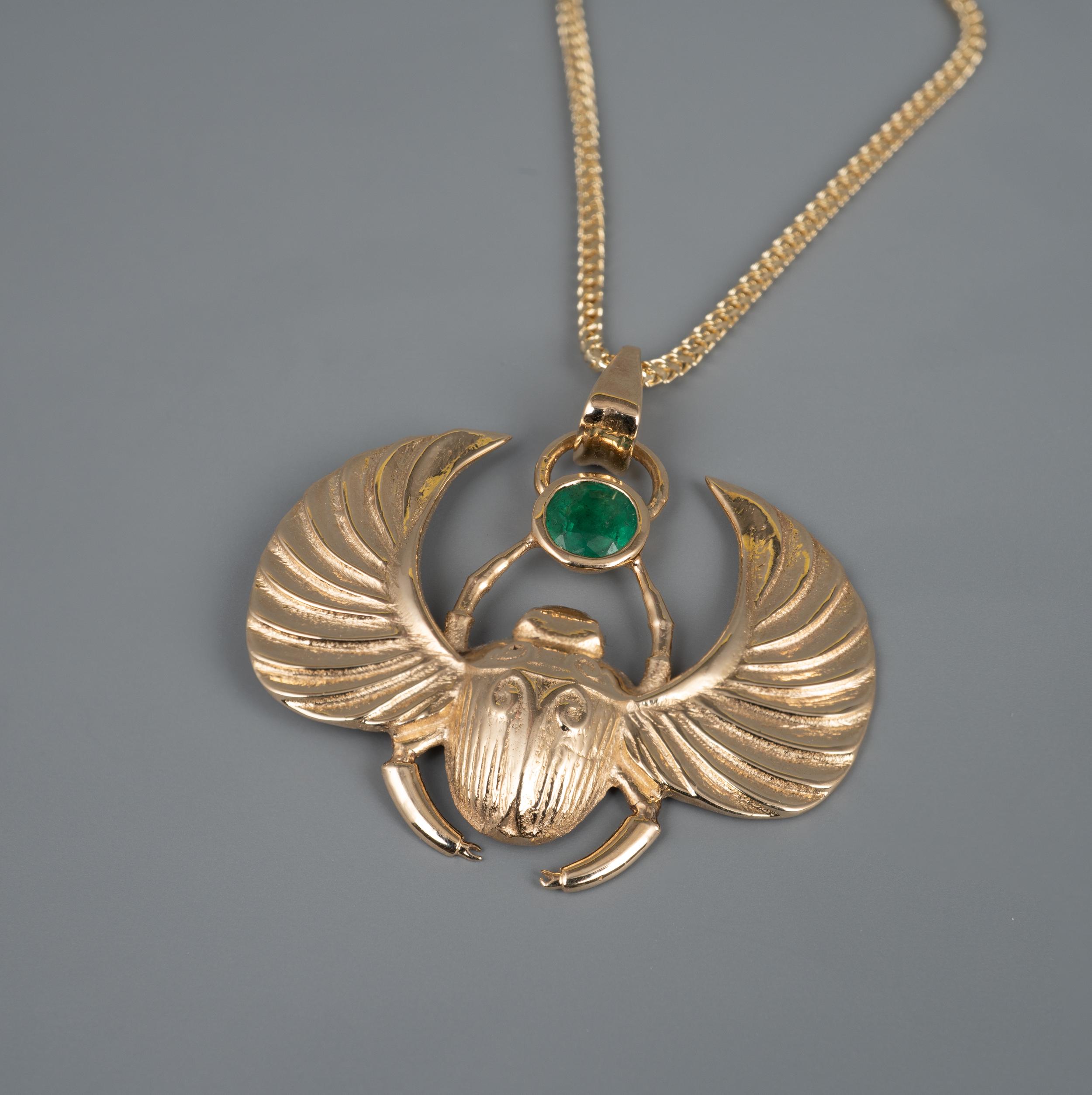 This Egyptian revival Winged Scarab Beetle pendant features a beautiful certified 0.41 carat round cut natural emerald gemstone. 

The custom made his piece displays full UK hallmarks and is expertly modelled with textured detail to the body and
