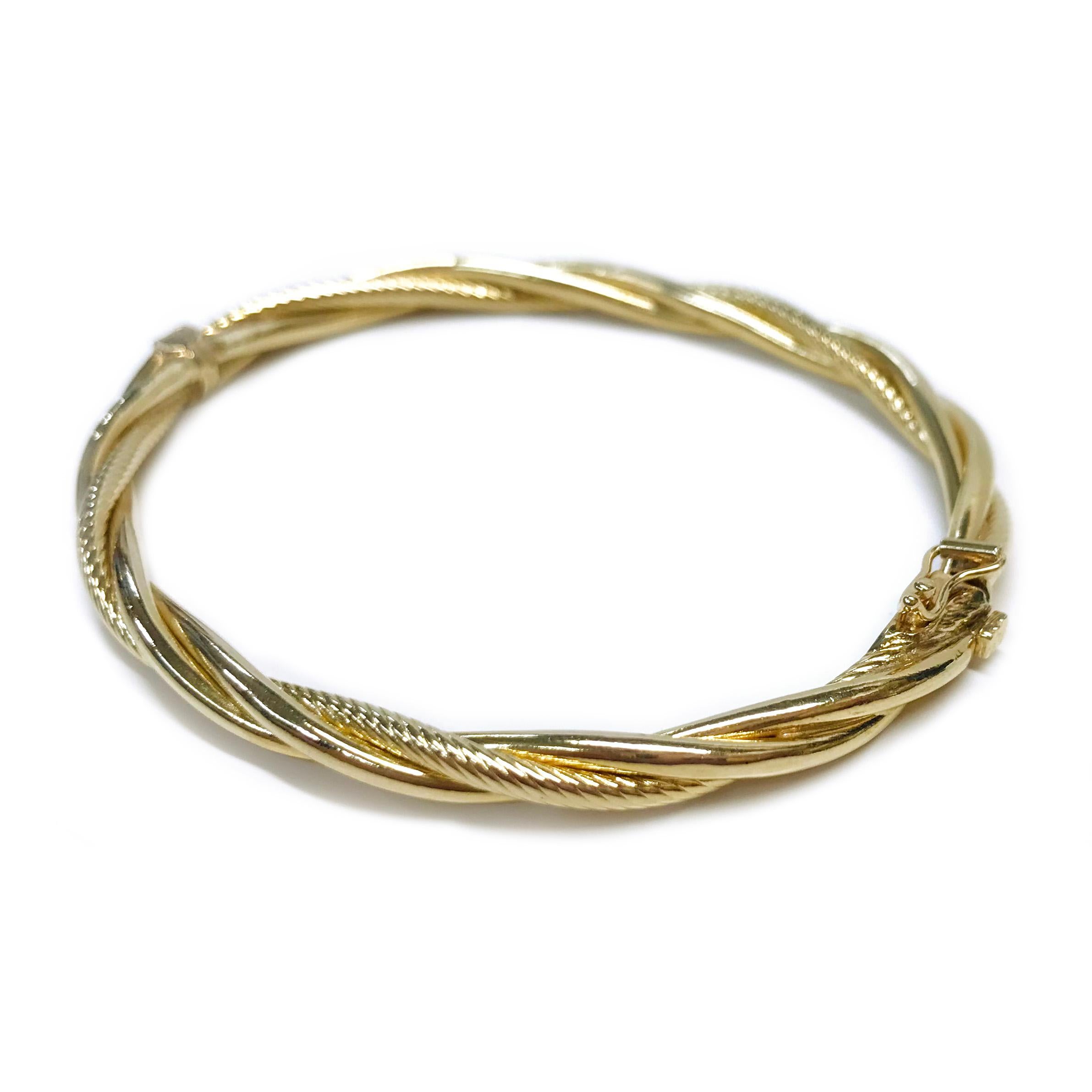 14 Karat Hinged Twisted Bangle Bracelet. The bangle consists of two smooth shiny tubes and one textured rope-style tube twisted to create the bracelet. The bangle is 2.75mm wide with one safety-eight. The bracelet is 2.5