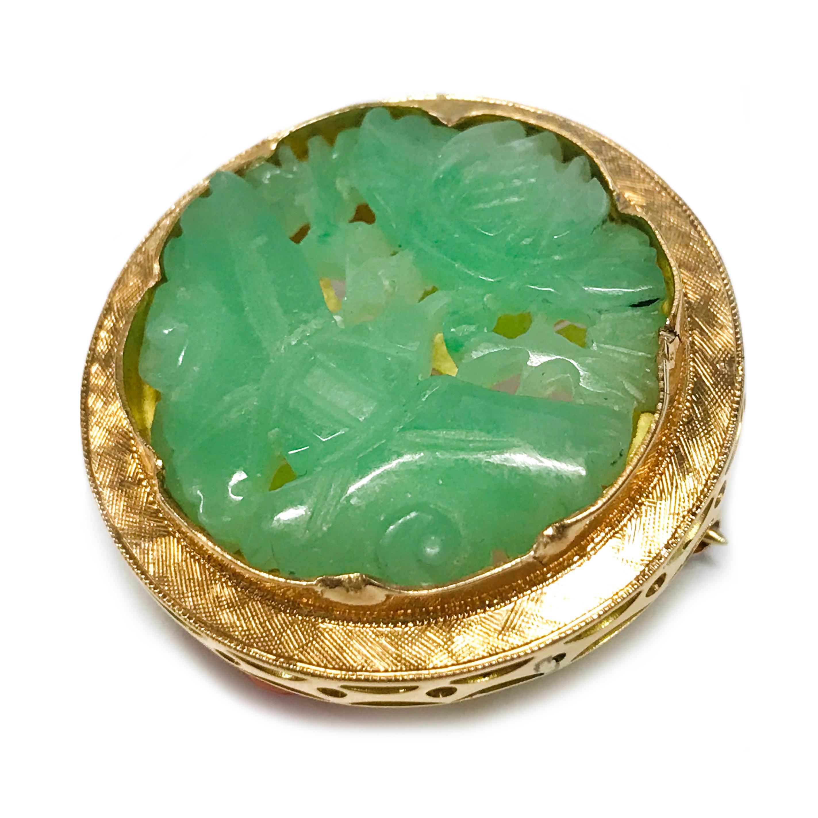 14 Karat Jade Coral Brooch. This brooch features a carved green Jade bezel-set in a decorative gold setting. The carved Jade is an image of a butterfly with its wings outspread and a lotus flower above. There is a Florentine finish along the bezel