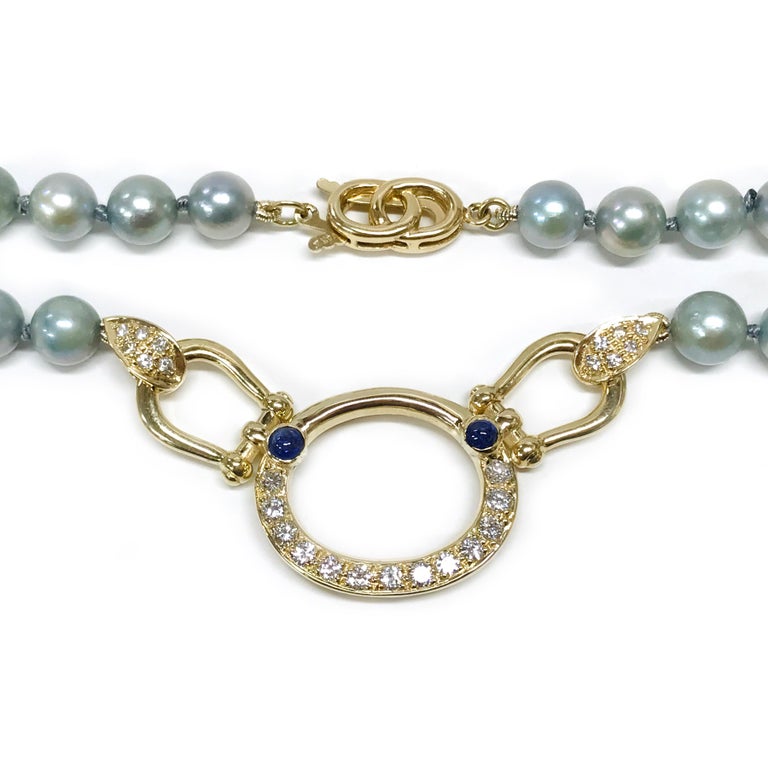 14 Karat Pearl Diamond Sapphire Necklace. The necklace feature forty-eight bluish-gray pearls with blue sapphire beads and an oval gold pendant. The pendant is shiny gold on the top portion and a bezel-set blue sapphire cabochon on both the left and