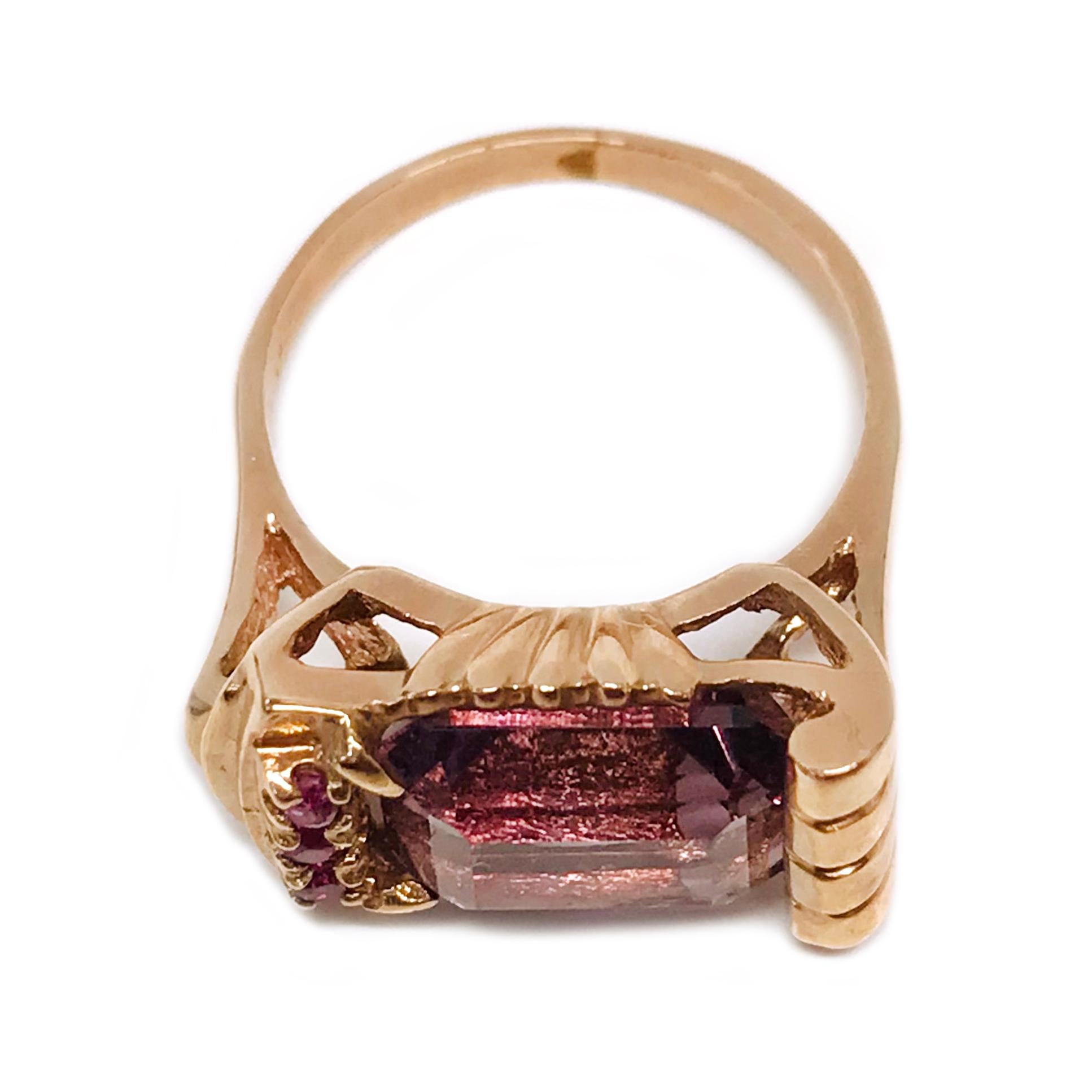 14 Karat Rose Gold Amethyst Ruby Ring. The ring features a step-cut 10 x 8mm Amethyst and three small round Rubies vertically set on one side. The other side has four gold upward scrolls adorning the side of the Amethyst. Stamped on the inside of