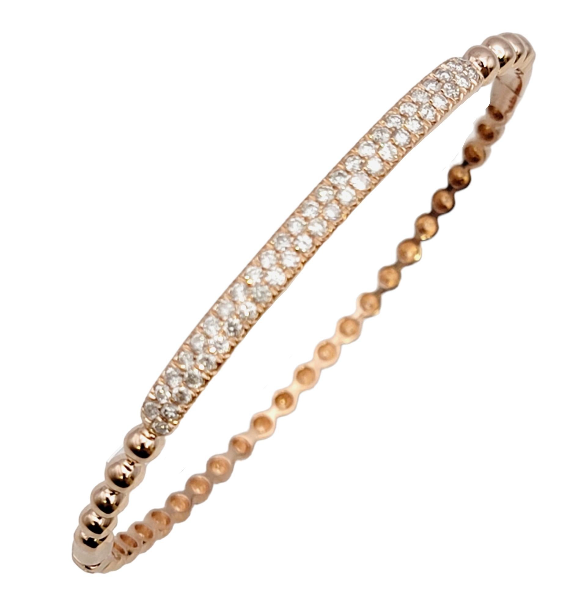 Contemporary bangle bracelet in a 14K rose gold featuring a narrow bubble design. The top portion of the sleek bracelet is adorned with two elegant row of sparkling pave diamonds. Stack it with other bracelets for a modern look, or simply wear on