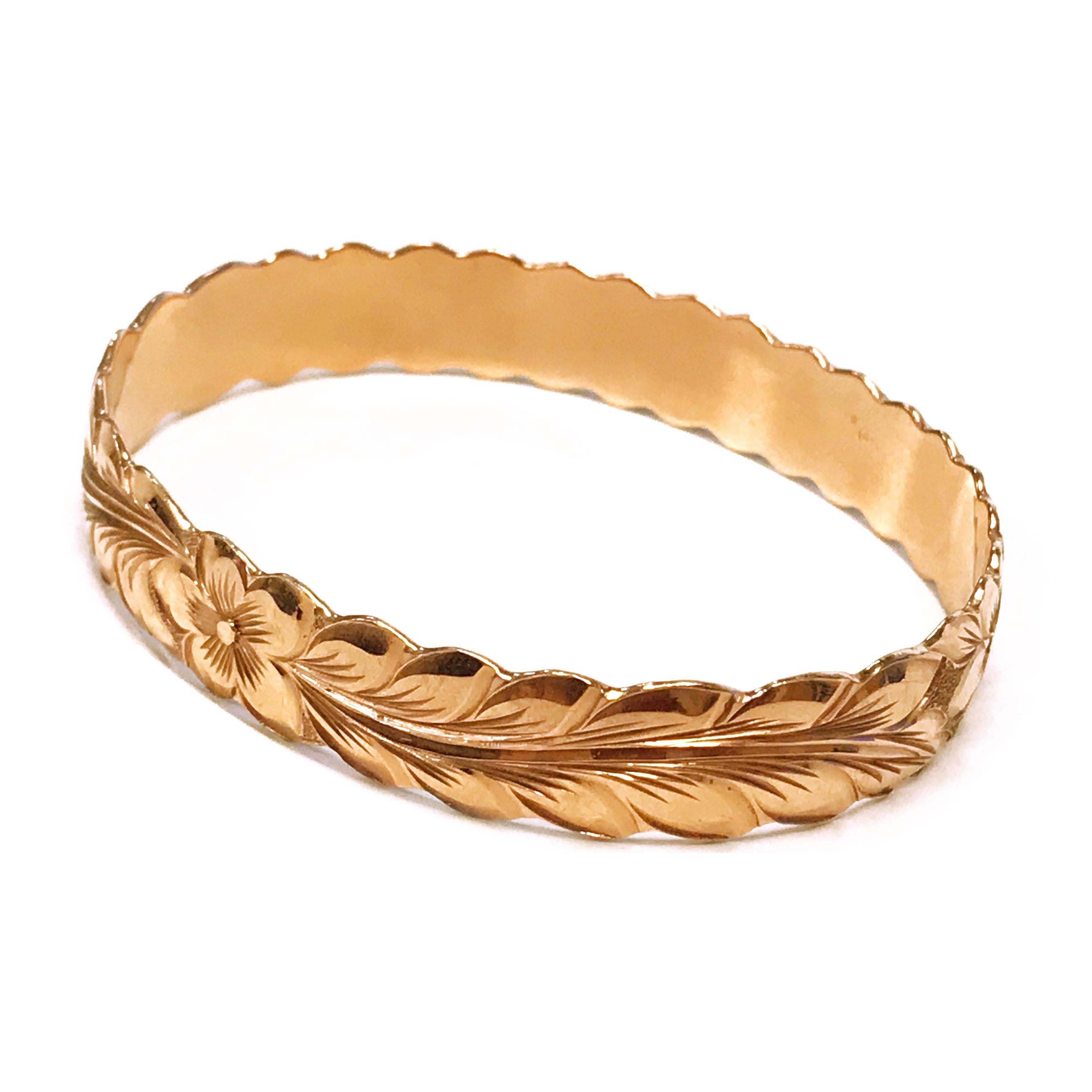 14 Karat Rose Gold Floral Bangle Bracelet. The Hawaiian bangle features a hand-engraved five-petal Plumeria flower at the center of one side with leaves encompassing the side of the bangle and eight Plumeria flowers on the other side, smooth finish