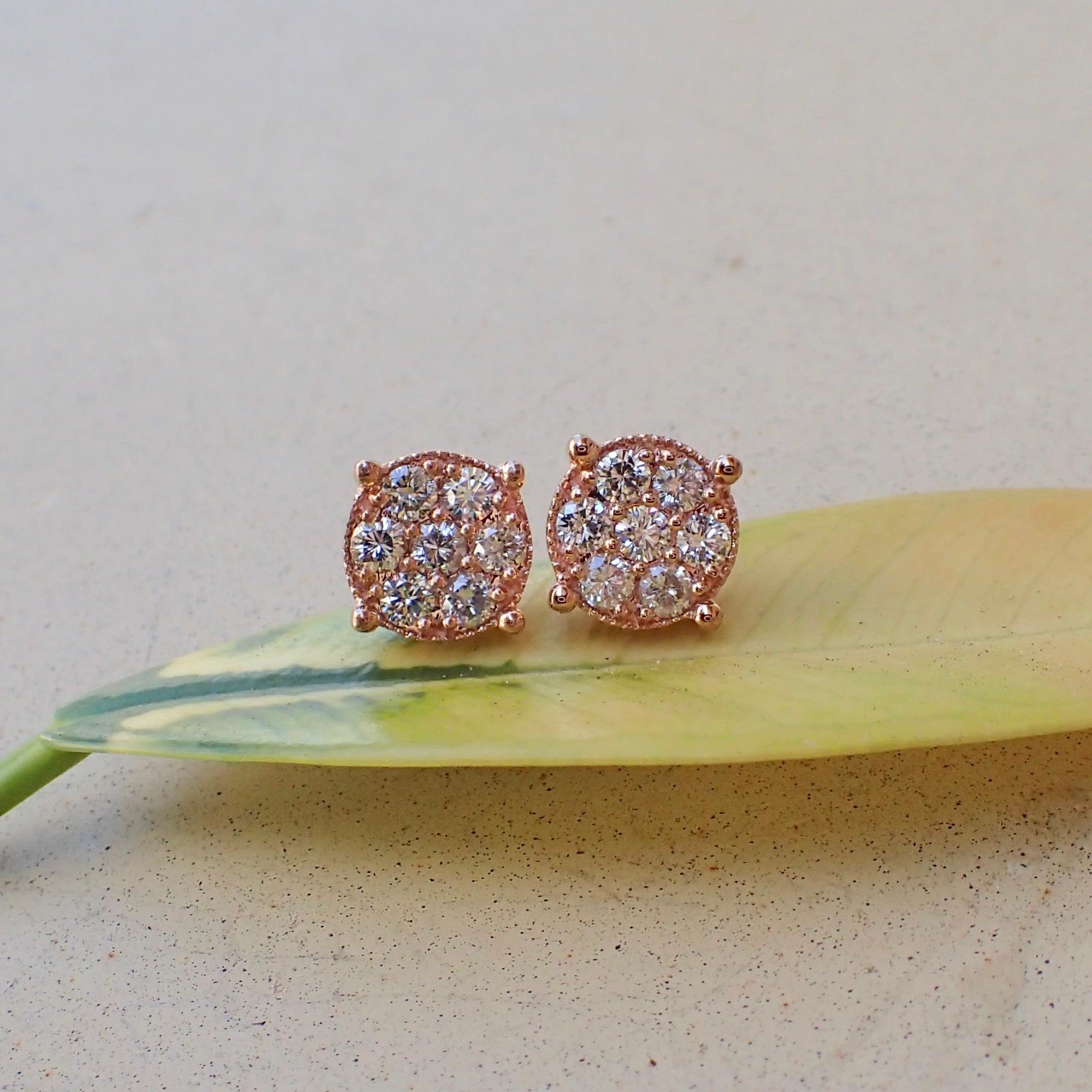 A pair of 14k rose gold earrings are prong set with two (2) Round Brilliant Cut diamonds measuring 2.6mm x 2.6mm that weigh a total of 0.14 carats with Cold Grade H and Clarity Grade VS-SI and surrounding the center stones are twelve (12) prong set