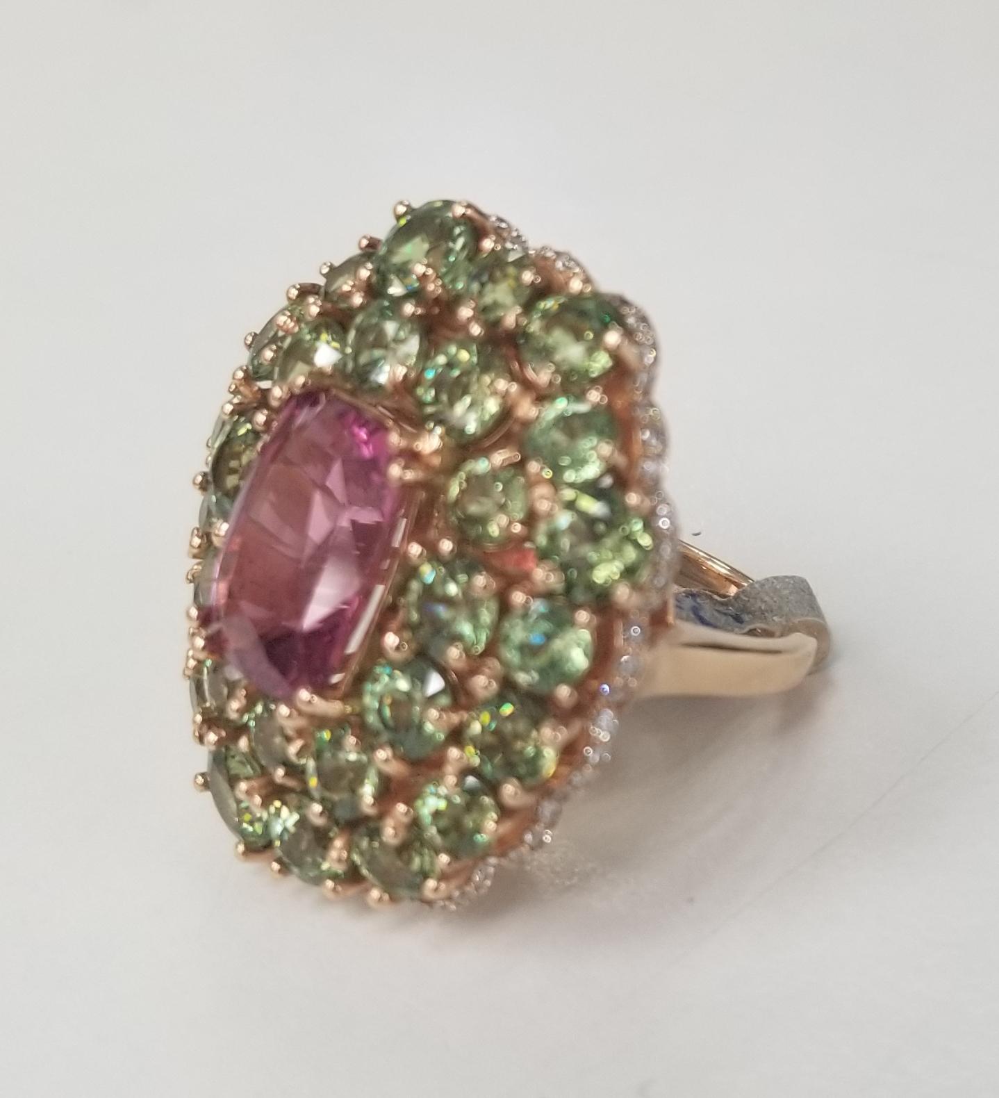 14 karat rose Pink Spinel and Demantoid with diamond edge ring, containing 1 cushion cut pink spinel weighing and 29 round green demantoid weighing 12.00cts. all stones are of gem quality.  Also 74 round full cut diamonds of very fine quality