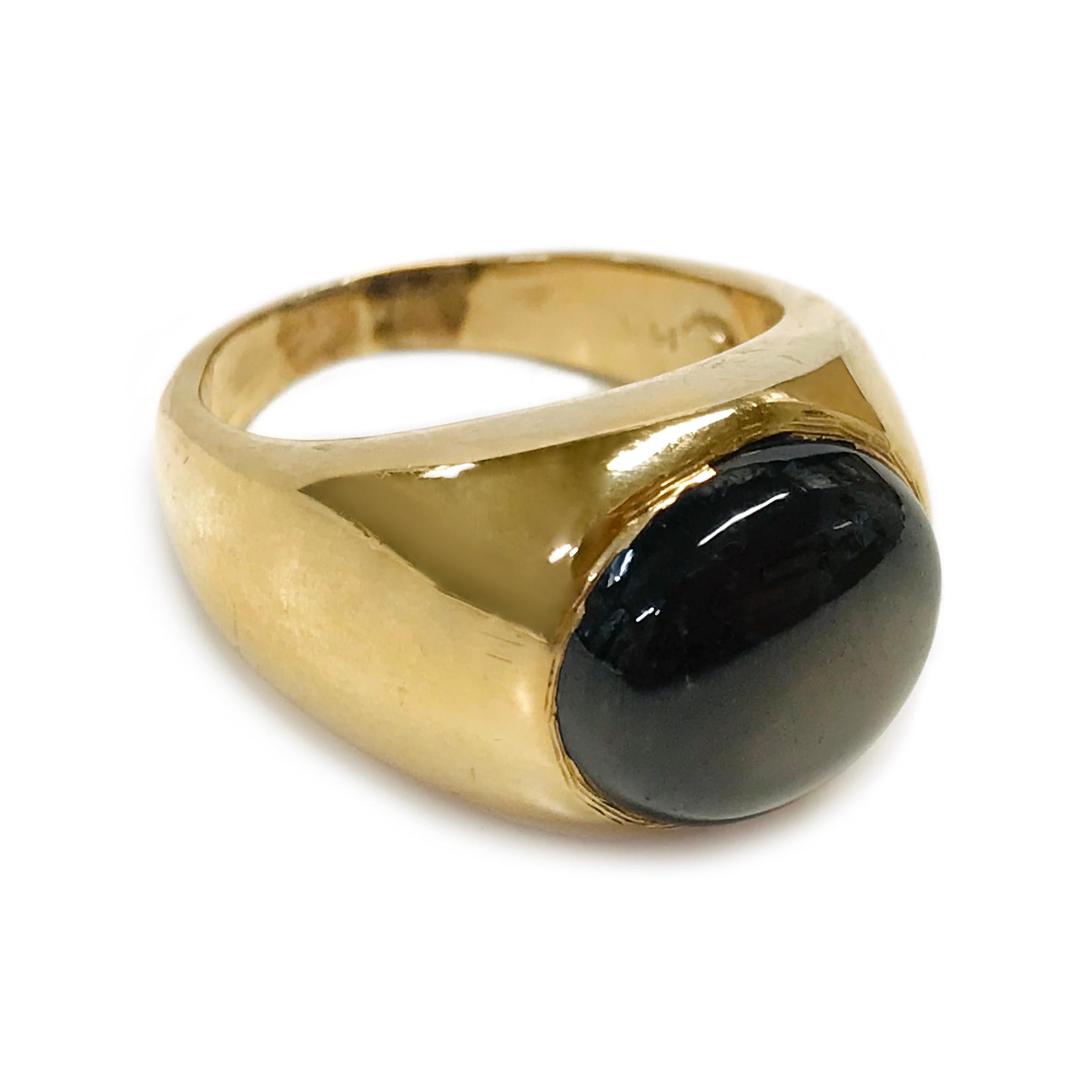 14 Karat Round Black Star Sapphire Ring. The ring features a bezel-set round black star sapphire. The six-star sapphire has great presence with light. The sapphire measures 12mm and the ring size is 6 3/4. The ring has a smooth shiny finish with a