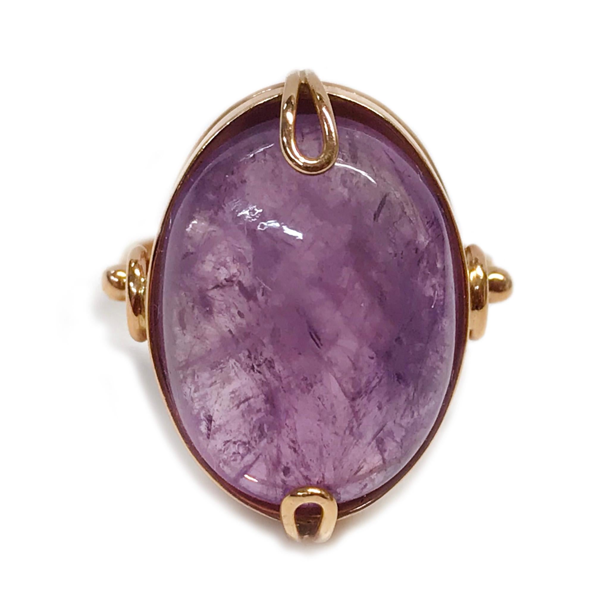 14 Karat Russian Rose Gold Amethyst Ring. The ring features a bezel-set 15.0ct oval cabochon Amethyst. The handmade ring also contains custom looped prongs and a simple wire detail that is attached to the bezel and band. Stamped on the inside of the