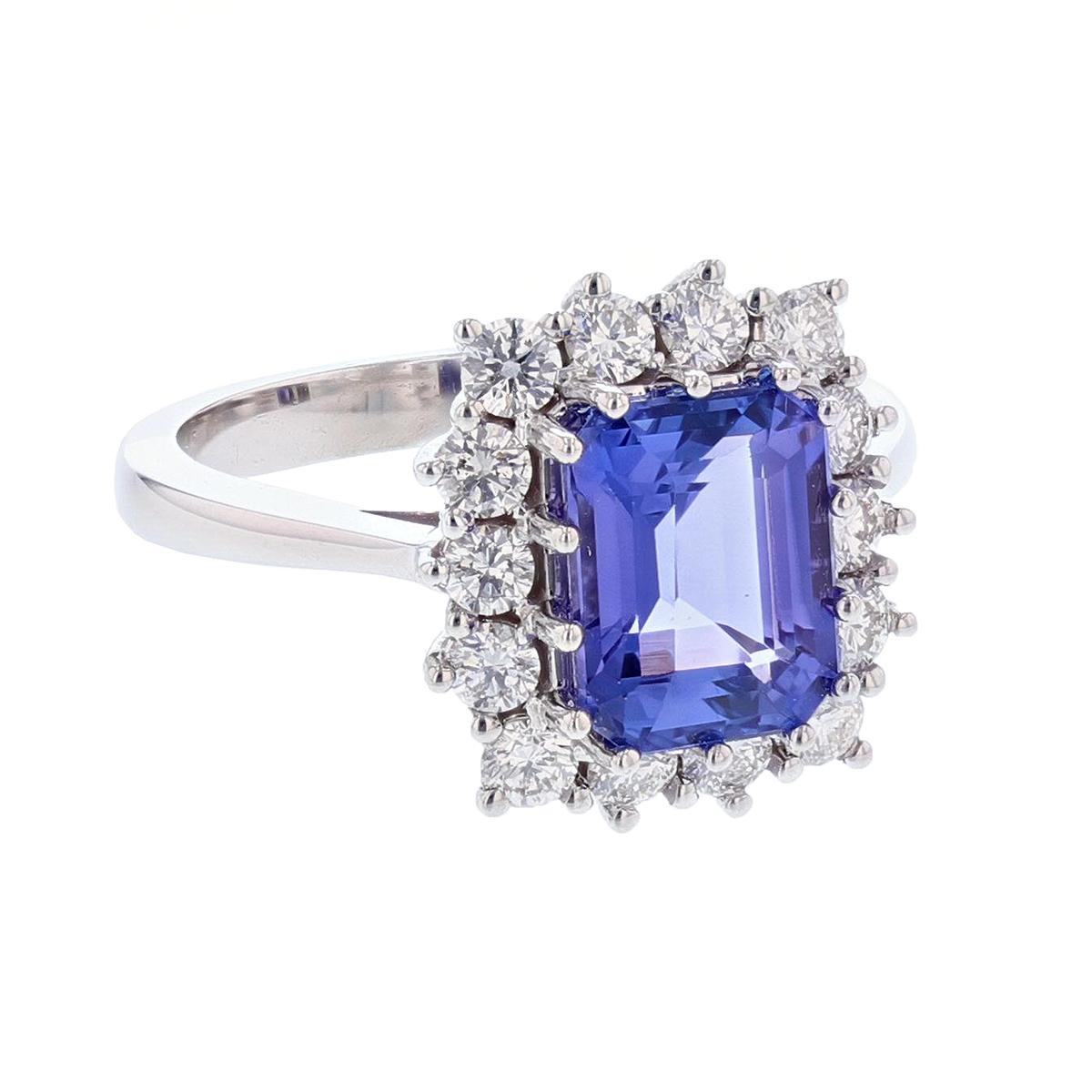 This ring is made in 14 karat white gold. The center stone is an Emerald cut Tanzanite weighing 2.88 carats and is prong set. The mounting features 14 round cut, prong set diamonds weighing 0.76 carats.