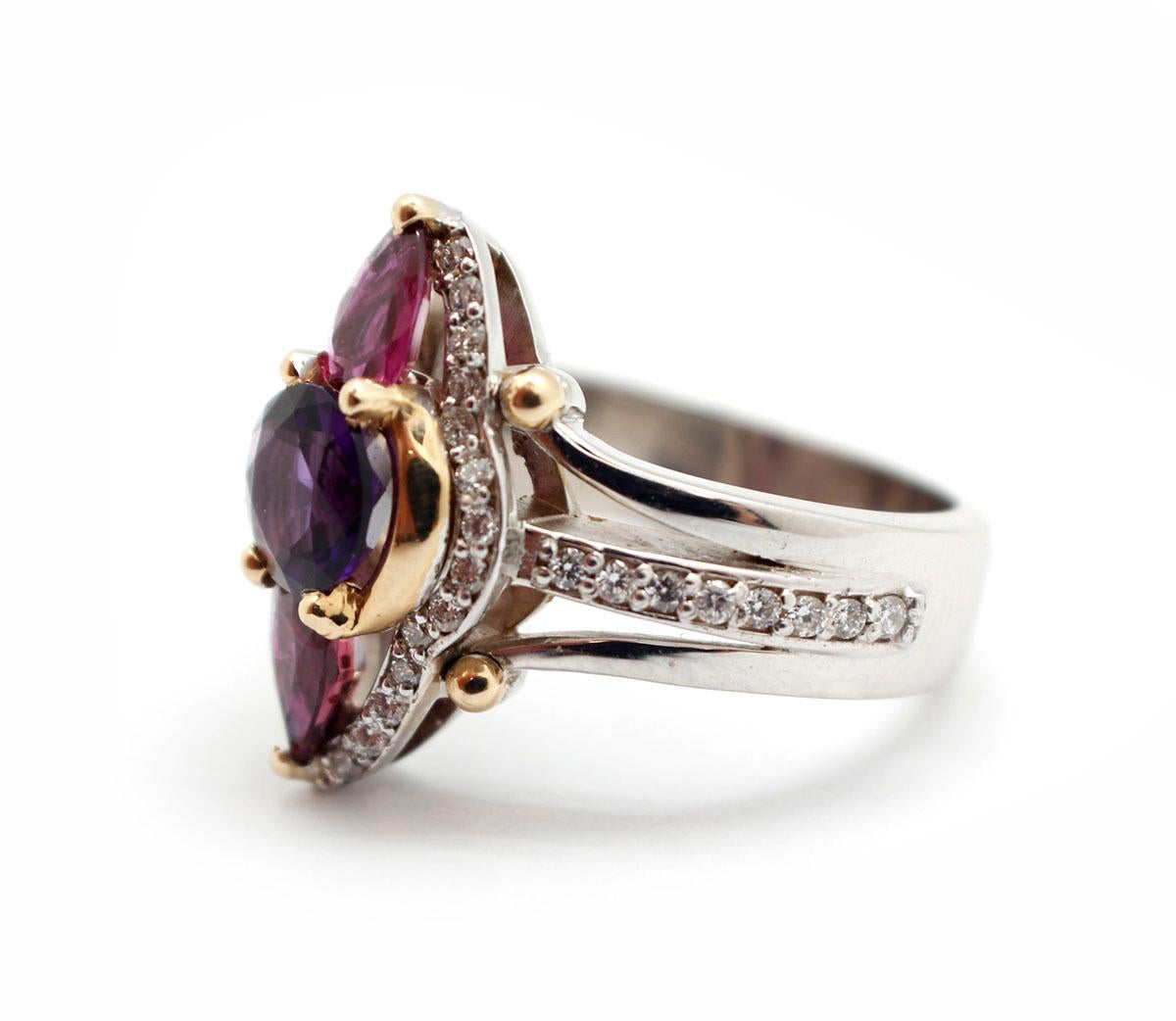This beautiful cocktail ring is made in 14k white gold and set with dazzling gemstones. A single round-cut amethyst sits in the center with pear-cut garnets on either side of it. The rest of the ring is set in round diamonds for a total weight of