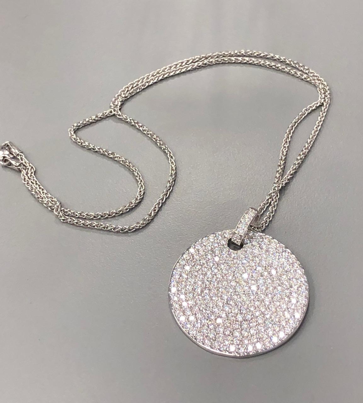 The gorgeous diamond pave encrusted disc measures 1.5 inches in diameter and is suspended from a 20 inch braided wheat style chain. It is pave set with 8.03 carats of full cut round diamonds near colorless range predominantly SI Clarity. The piece