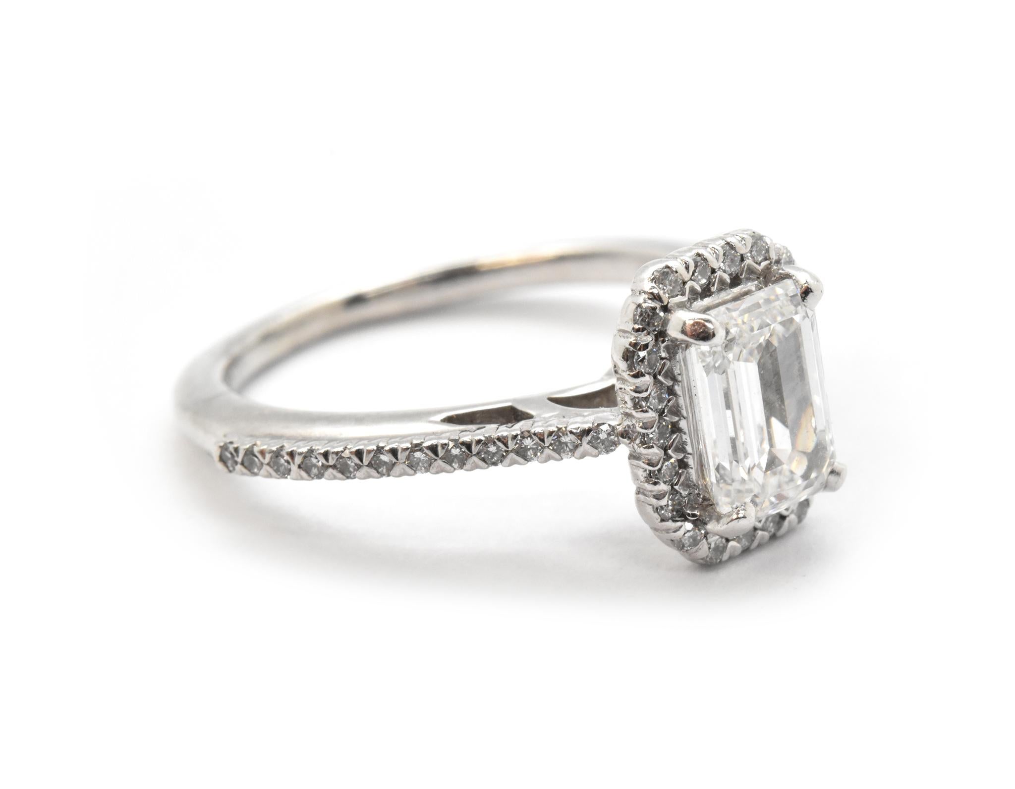 This beautiful engagement ring is made in 14k white gold. It features a 1.07ct emerald-cut diamond surrounded by round diamond accents. The center diamond is graded F in color and VS1 in clarity. The diamond is GIA-certified. The accent diamonds