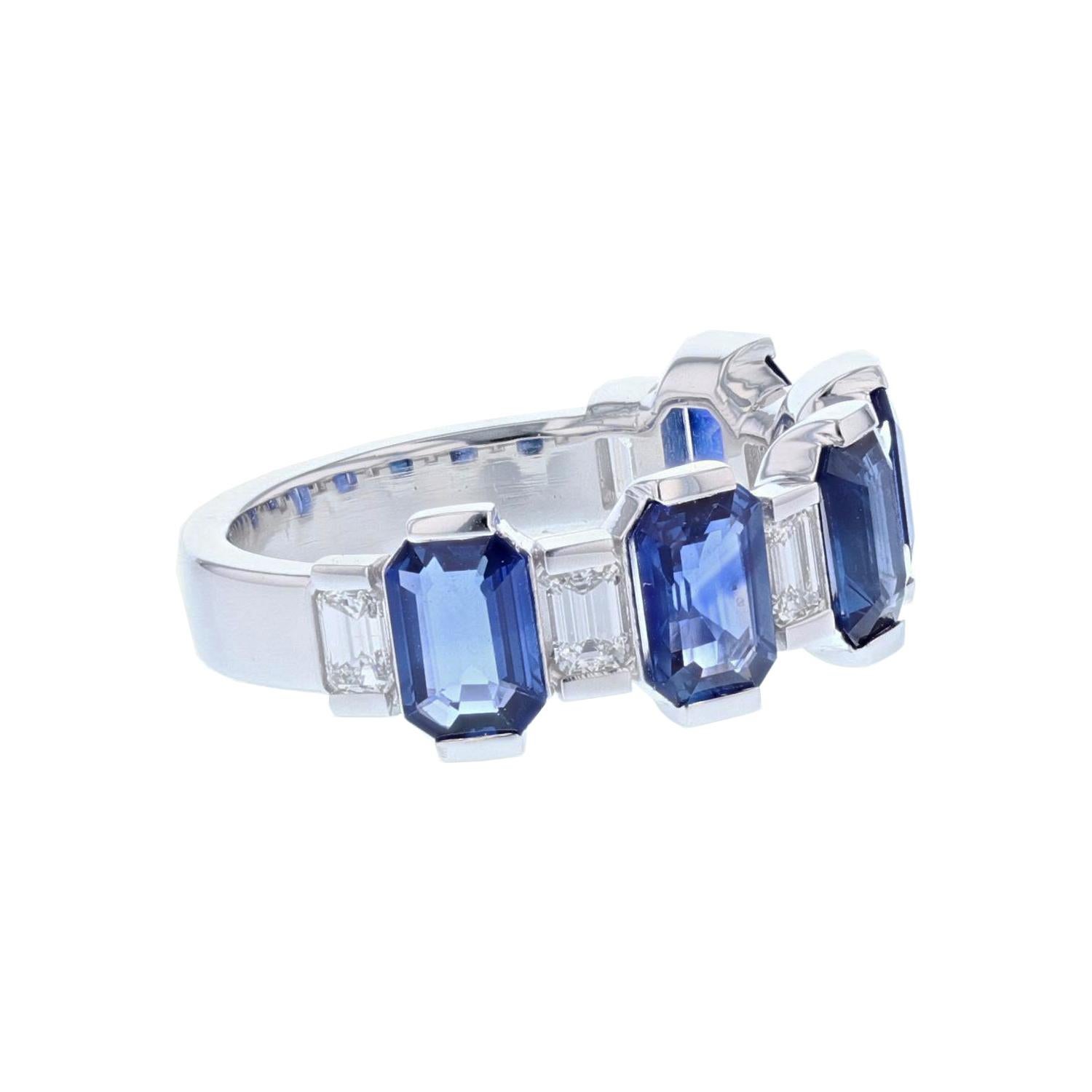 This ring is made in 14 karat white gold featuring five Emerald cut, channel set Blue Sapphires weighing 3.19 carats and six Baguette cut,  prong set Diamonds weighing 0.58 carats and twelve Round cut, prong set Diamonds weighing 0.44 carats with a
