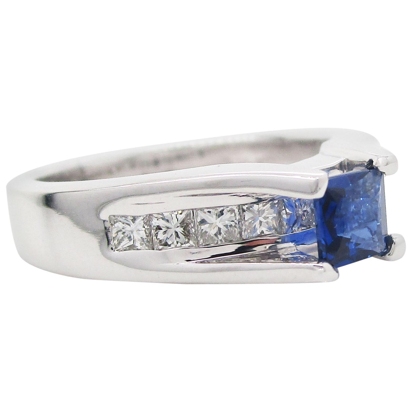 This is a magnificent ring in 14k white gold featuring a beautiful blue sapphire center and a row of channel-set diamonds. The sapphire center is a gorgeous rich blue stone whose hues are reminiscent of a velvety dusk sky. The sapphire is set over a