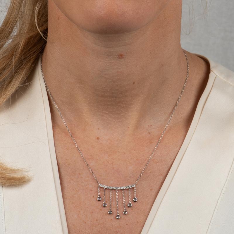 This unique necklace features a pave diamond bar with seven bezel set diamonds that dangle set in 14 karat white gold. The 18