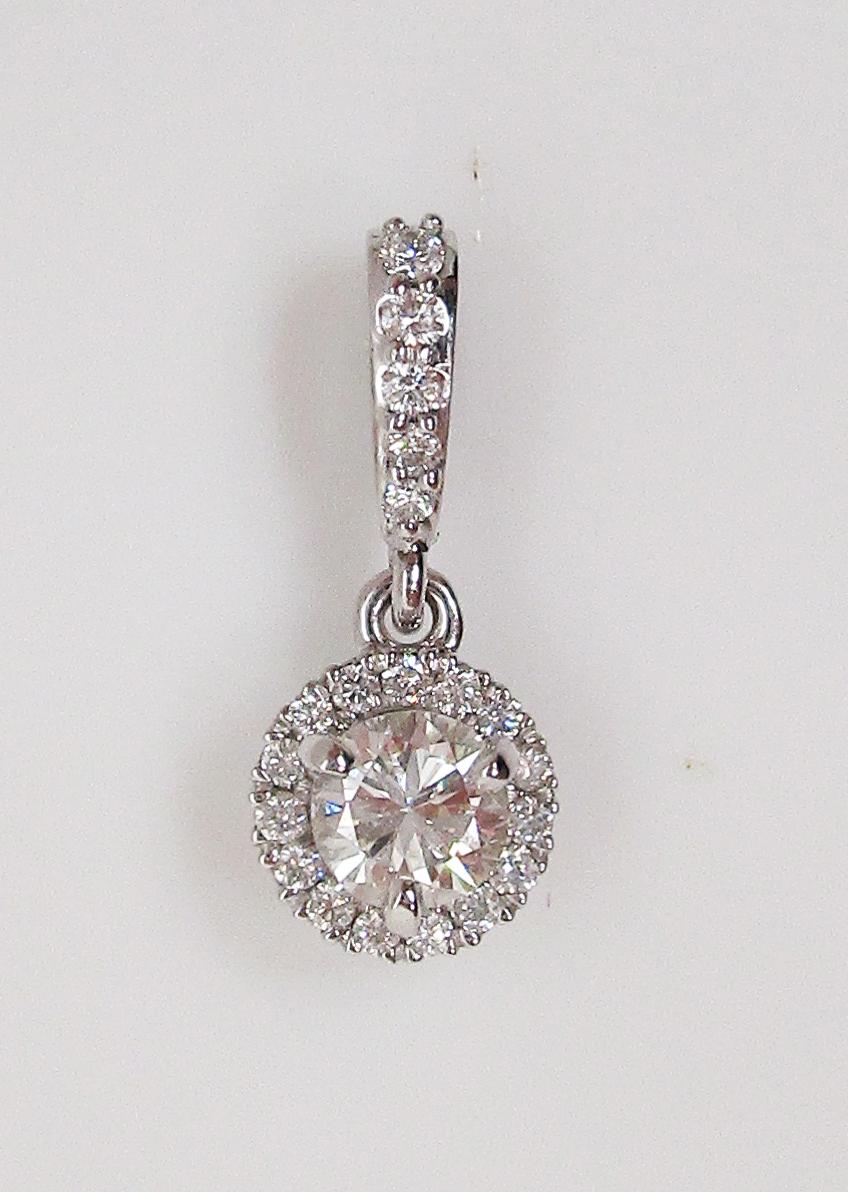 This is a gorgeous pendant in 14k white gold featuring a diamond center stone surrounded by a diamond halo! The simple, elegant design puts the beautiful diamonds on full display. This beautiful pendant would be stunning on a matching white chain or