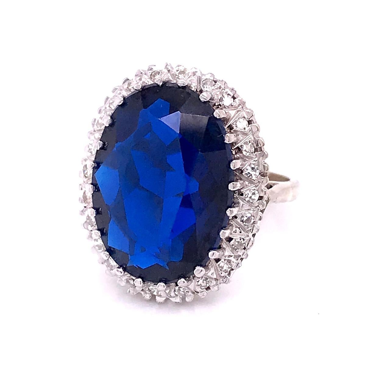 A very fine gold and multi-gemstone cocktail ring.

In 14k white gold. 

Set with a large deep blue oval-cut topaz surrounded by a halo of 24 small round-cut diamonds.

Simply an eye-catching ring that is fun to wear and makes you