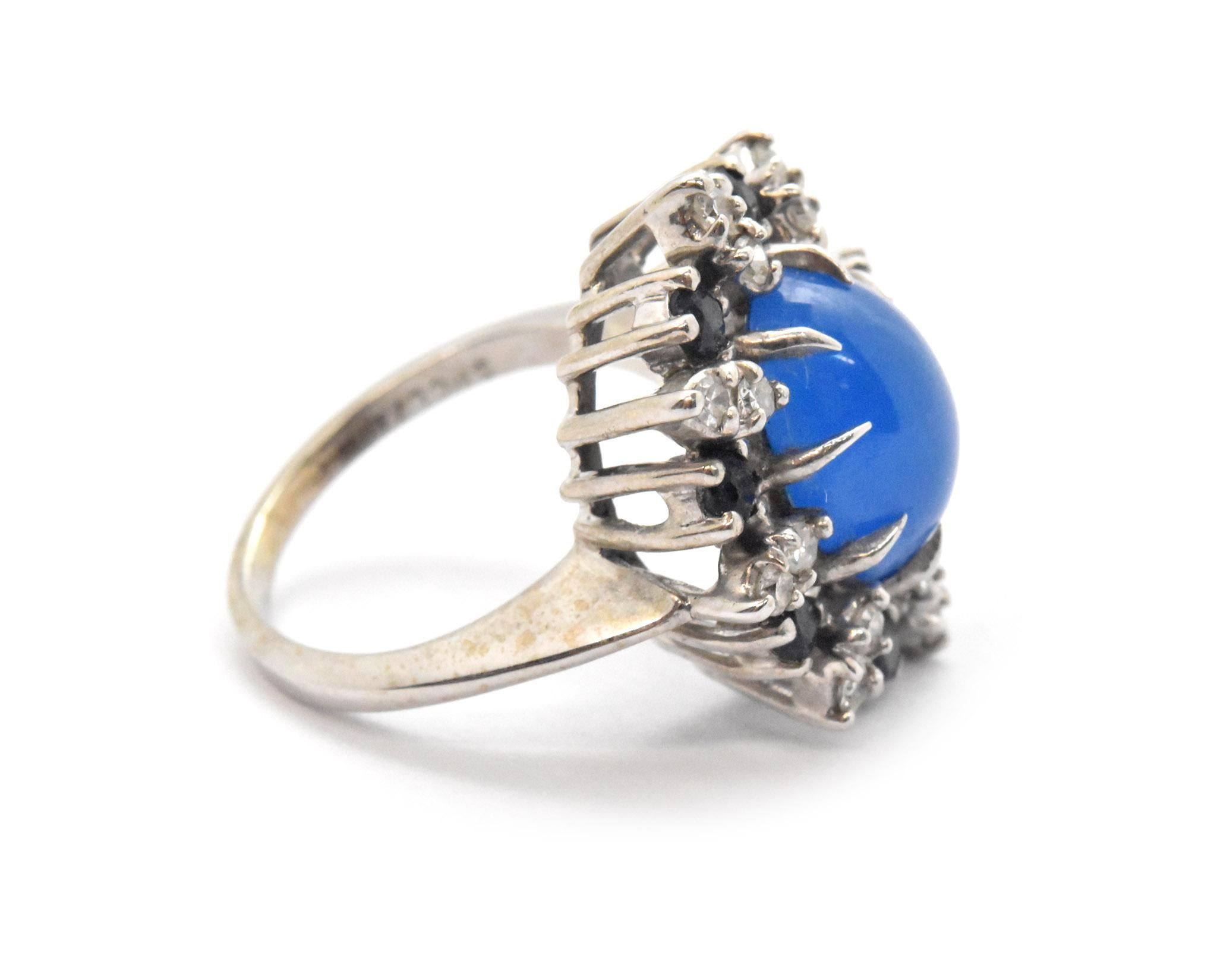 This ring features an oval blue cabochon in the center of a halo of diamonds and sapphires. The diamonds have a total weight of 0.16ct, and the sapphires have an additional weight of 0.24ct. The ring measures 19mm wide, and it weighs 5.1 grams. The