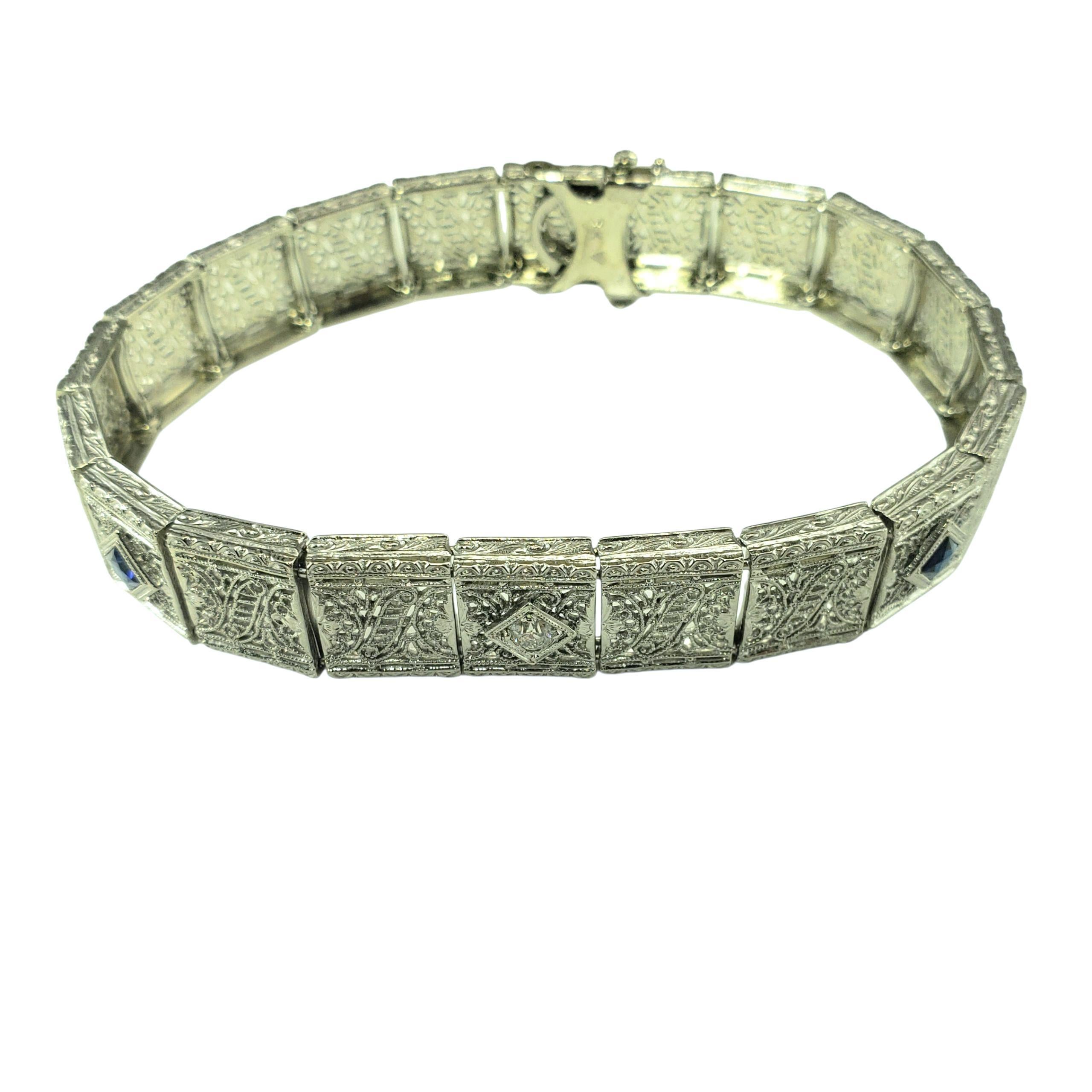 14K White Gold Filigree and Diamond Bracelet-

This elegant bracelet features intricate filigree craftsmanship in beautifully detailed 14K white gold. The centerpiece is a sparkling European cut diamond flanked by two vivid square cut blue stones,