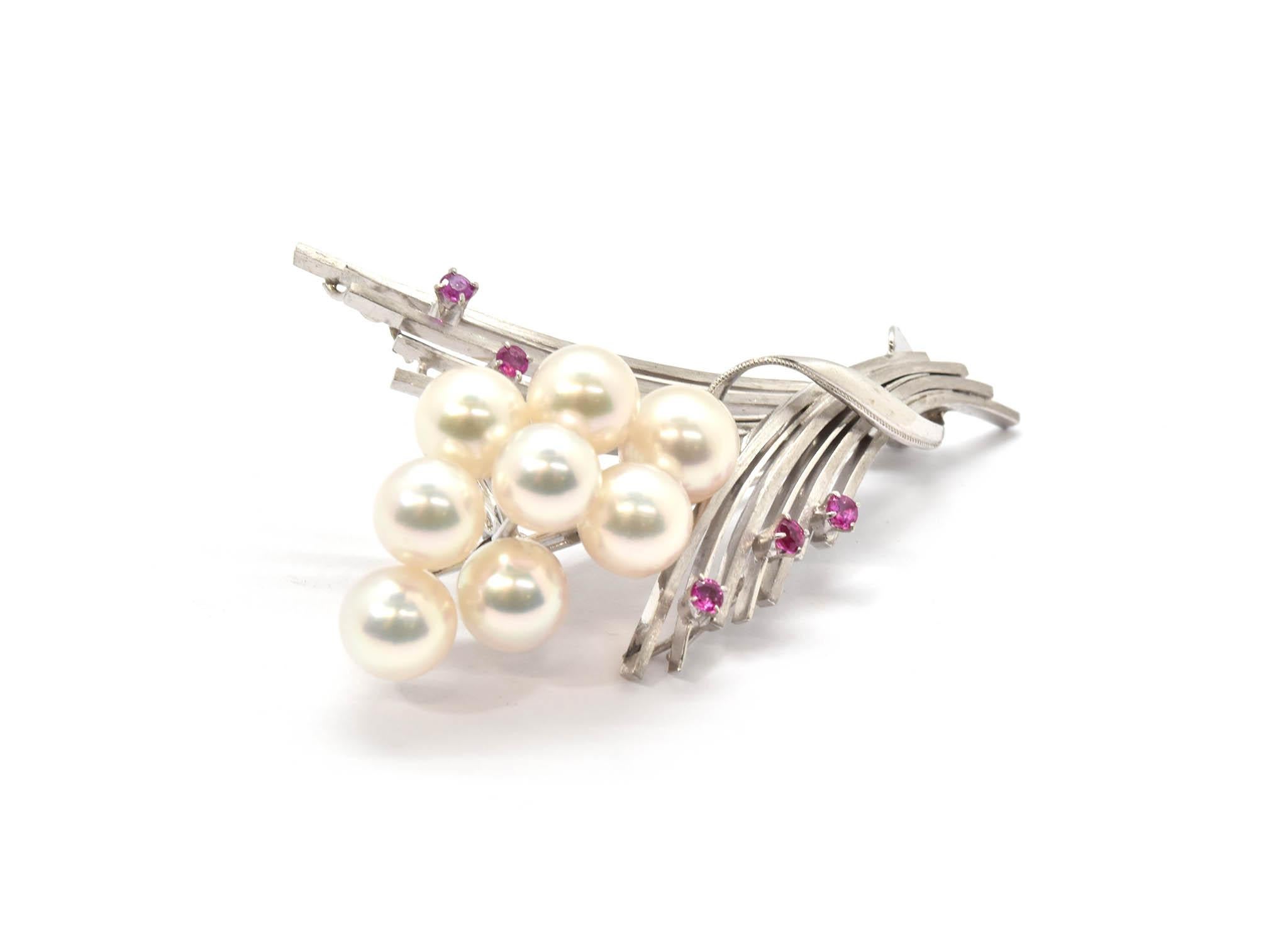This creatively made flower pin is made with style! This pin is designed with a fabulous high polished finish, with a wrapping design made with an etched trim and rubies set at the top of the white gold flower strands. Each pearl is mounted