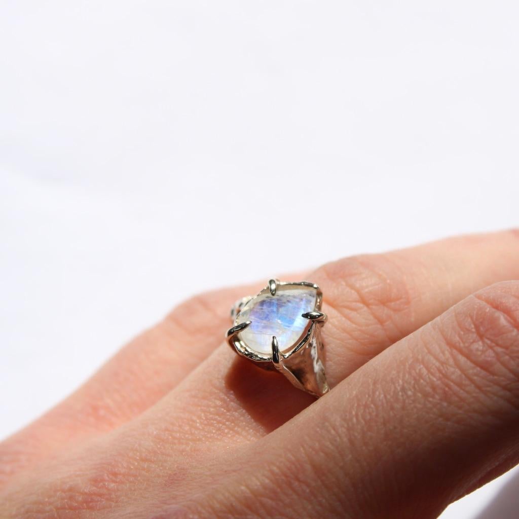 Handgeschnitzter Ring aus 14-karätigem Weißgold mit einem facettierten 10x7-mm-Regenbogen-Birnenmondstein. Dieses Stück wird auf Bestellung in Ihrer Größe angefertigt. Bitte rechnen Sie mit 3 Wochen Produktionszeit. 

Dieses Stück ist handgefertigt,