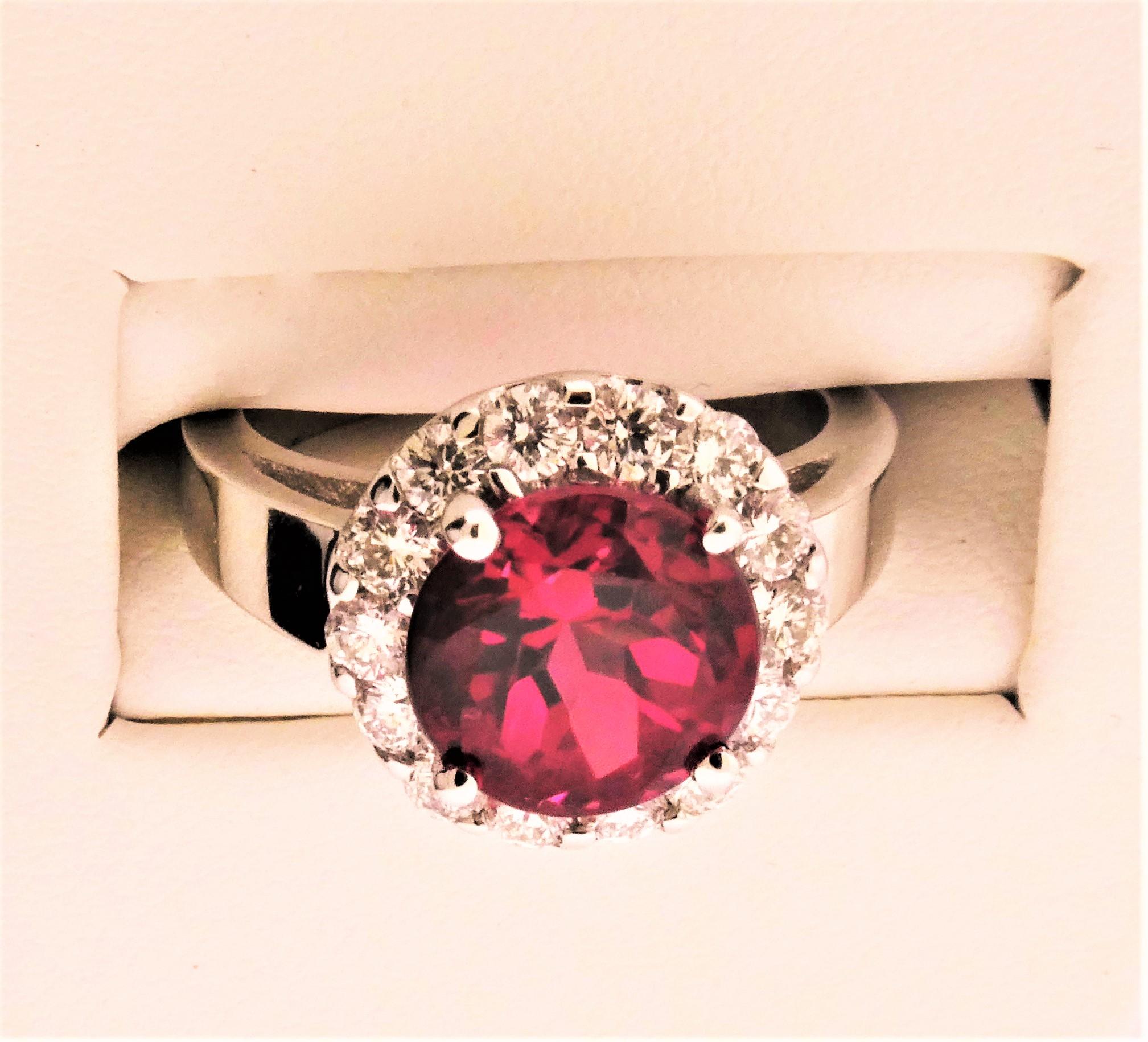Nestled inside a Halo of G-H Color VS Clarity Diamonds is a very bright and lively Red Tourmaline that weighs 3.21 carats. There are 14 matching Diamonds that form the Halo and weigh 0.78 carats. The entire mounting is made in 14 Karat White Gold