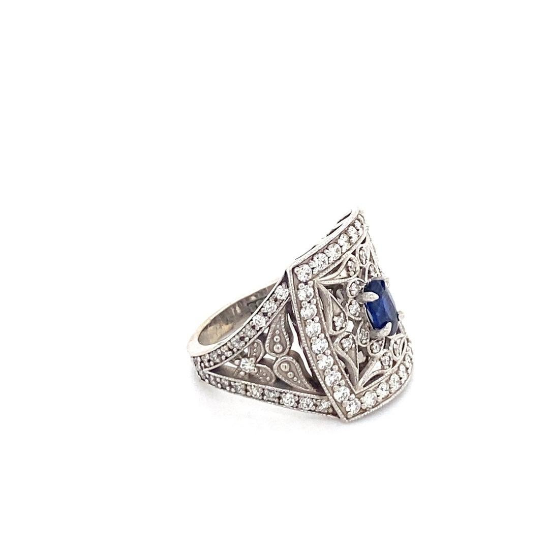 This stunning 14 karat white gold ring was custom made by our expert jewelers. The center stone is a blue sapphire surrounded by an intricate antique style. There is a total diamond weight of 1.30cttw. This ring is the perfect statement ring.