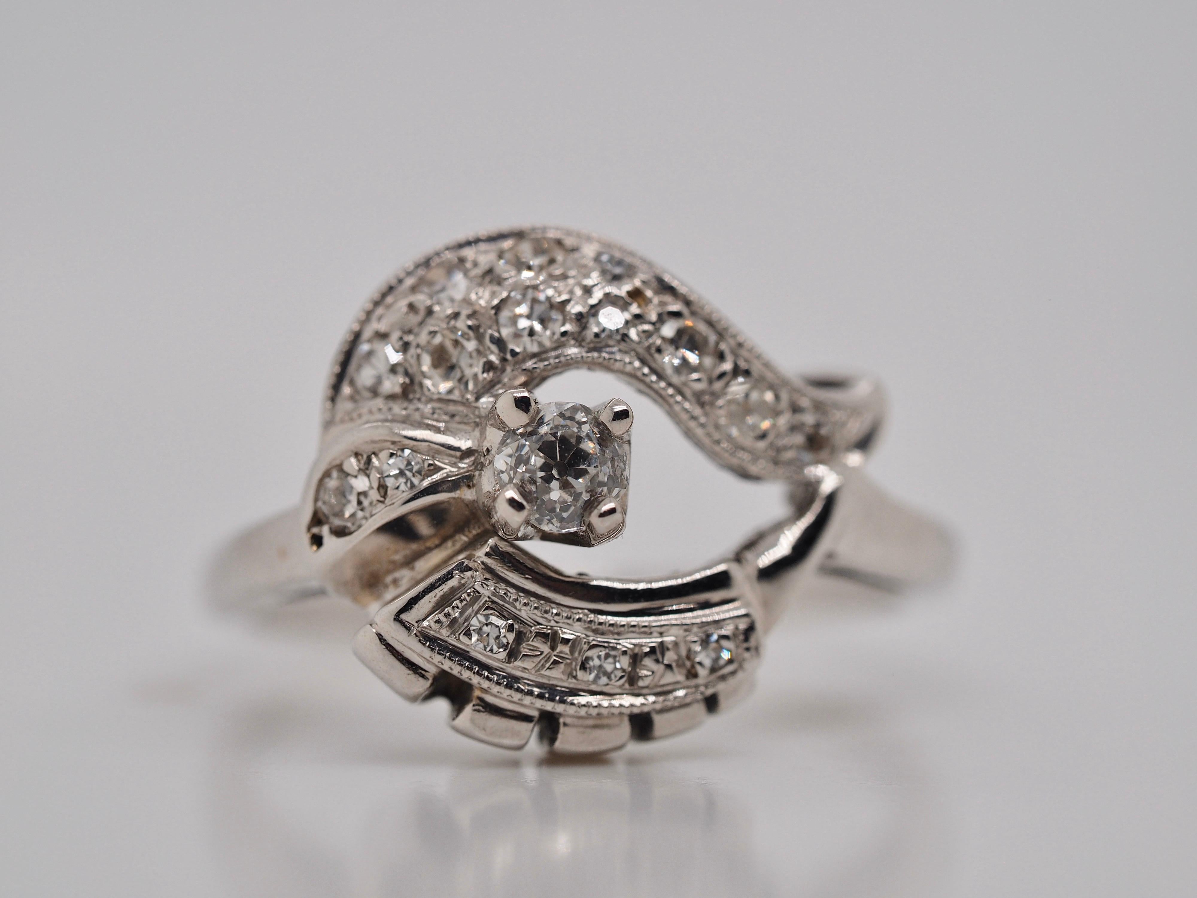 14 Karat White Gold Art Deco Vintage cocktail ring features an Old Mine Cut Diamond weighing  0.19 carats VS2 clarity, H-I in color. It is swirled by fifteen accented single cut Diamonds weighing approximately 0.15 carats total weight VS - I 1