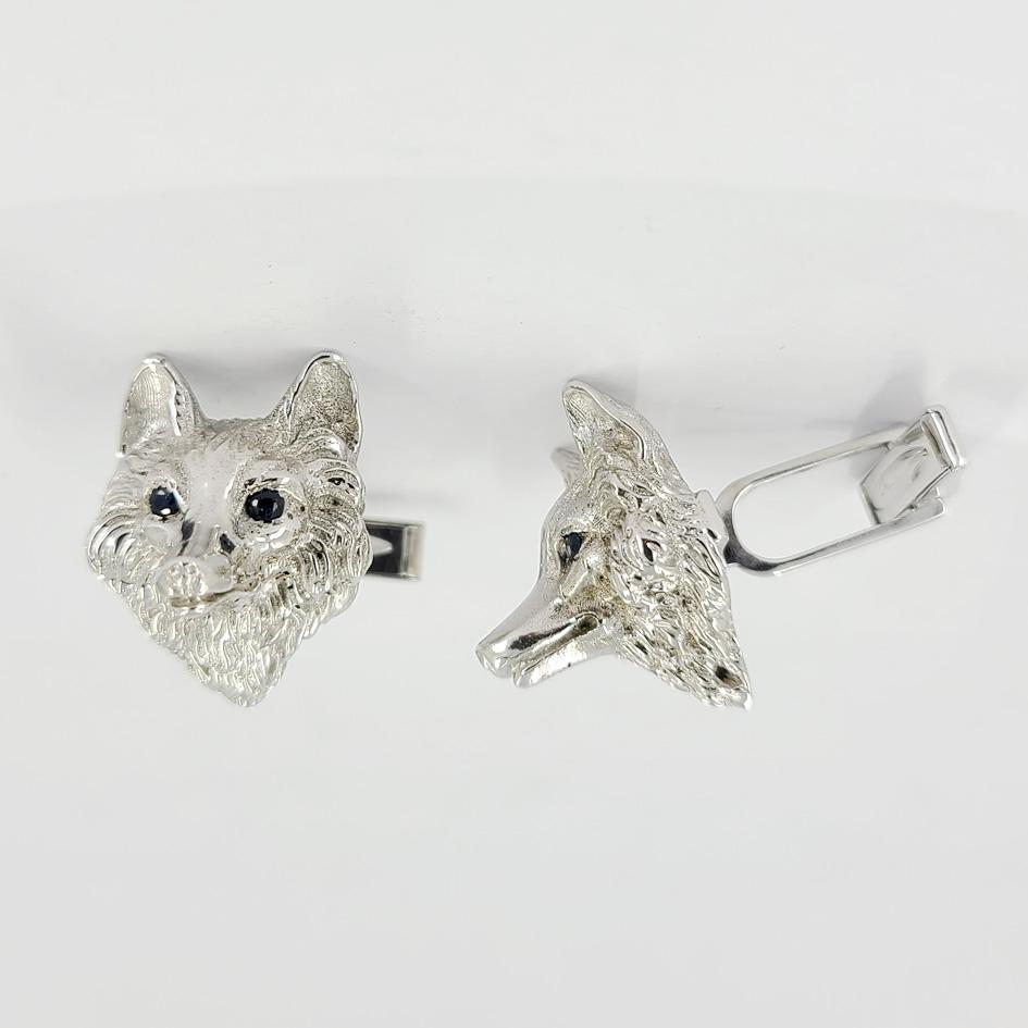 14 Karat White Gold Cufflinks Featuring A 3D Wolf Head Design With Sapphire Eyes Totaling 0.20 Carats. Finished Weight Is 24.5 Grams. Torpedo Hinged Backs.