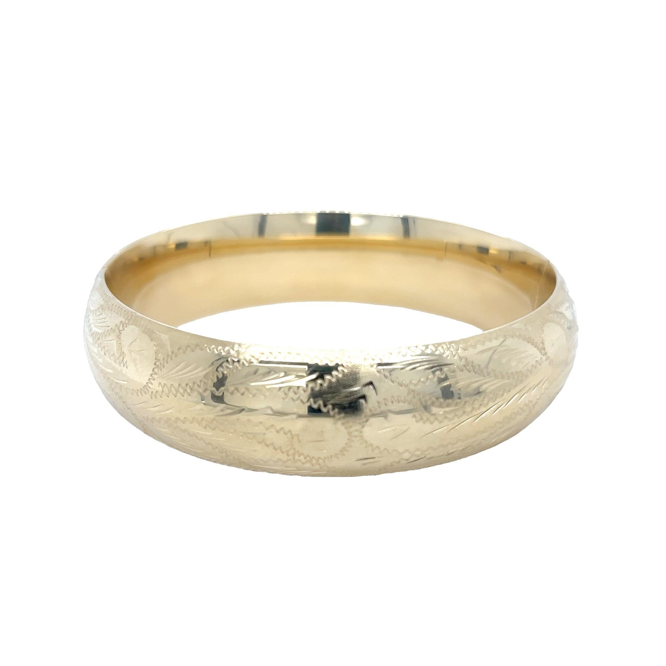 Timeless elegance meets bold craftsmanship in this 14 karat yellow gold engraved bangle bracelet. Measuring an impressive 17mm in width, this vintage-inspired piece features detailed hand-engraved accents that bring depth, texture, and classic