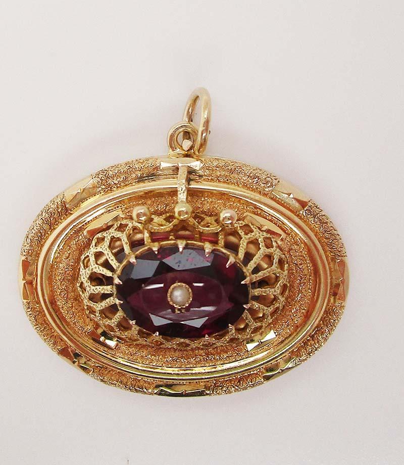 This is a gorgeous Victorian pendant in 14k yellow gold with a stunning cathedral style setting with a  red garnet at the center. The pendant has a subtly engraved border and an architectural center section that holds up a gorgeous gem-quality red