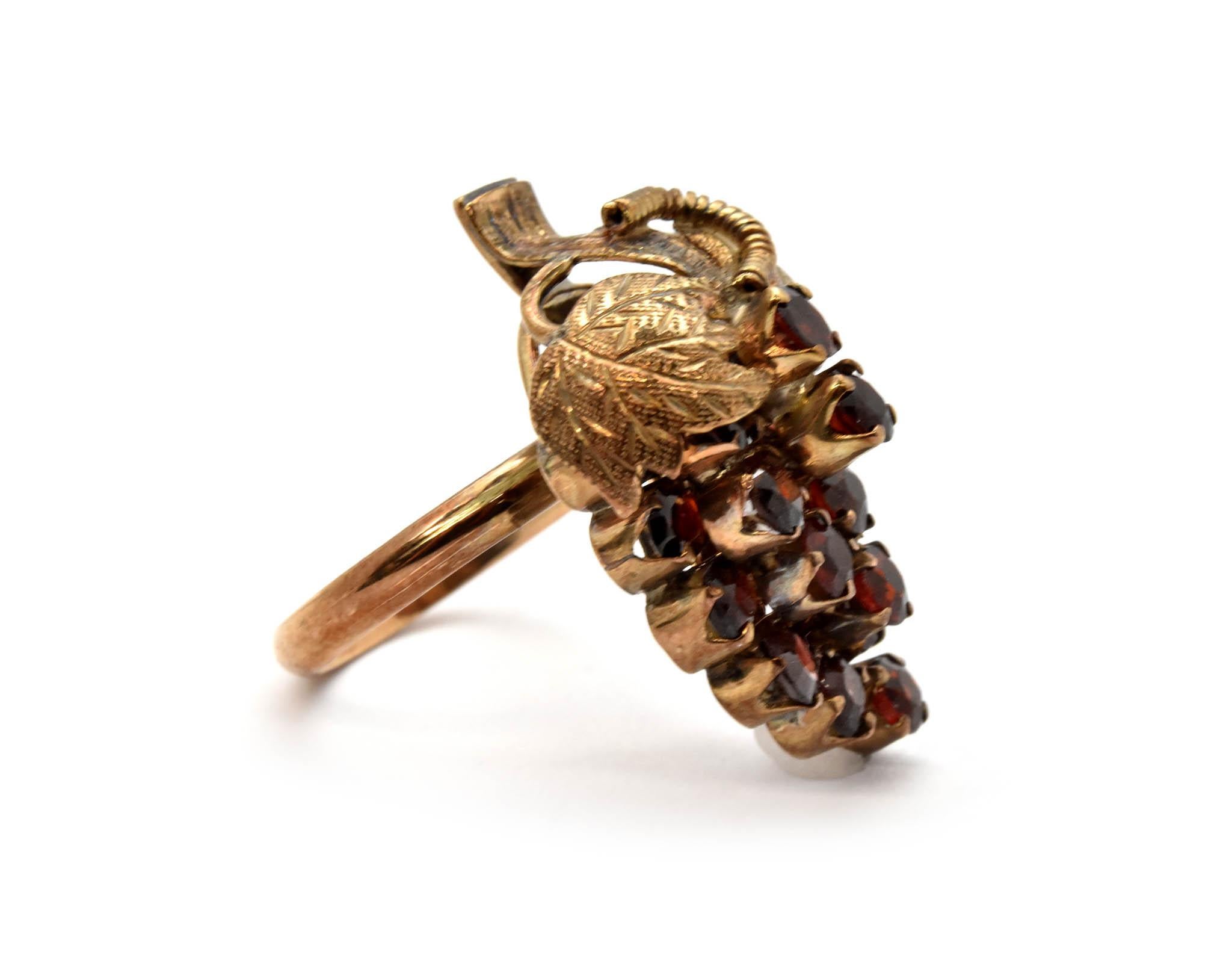 This fun ring is made in 14k yellow gold, and it features round red garnets in a grape bunch formation. The ring measures 27x19mm, and it weighs 4.9 grams. The ring is a size 5.5.