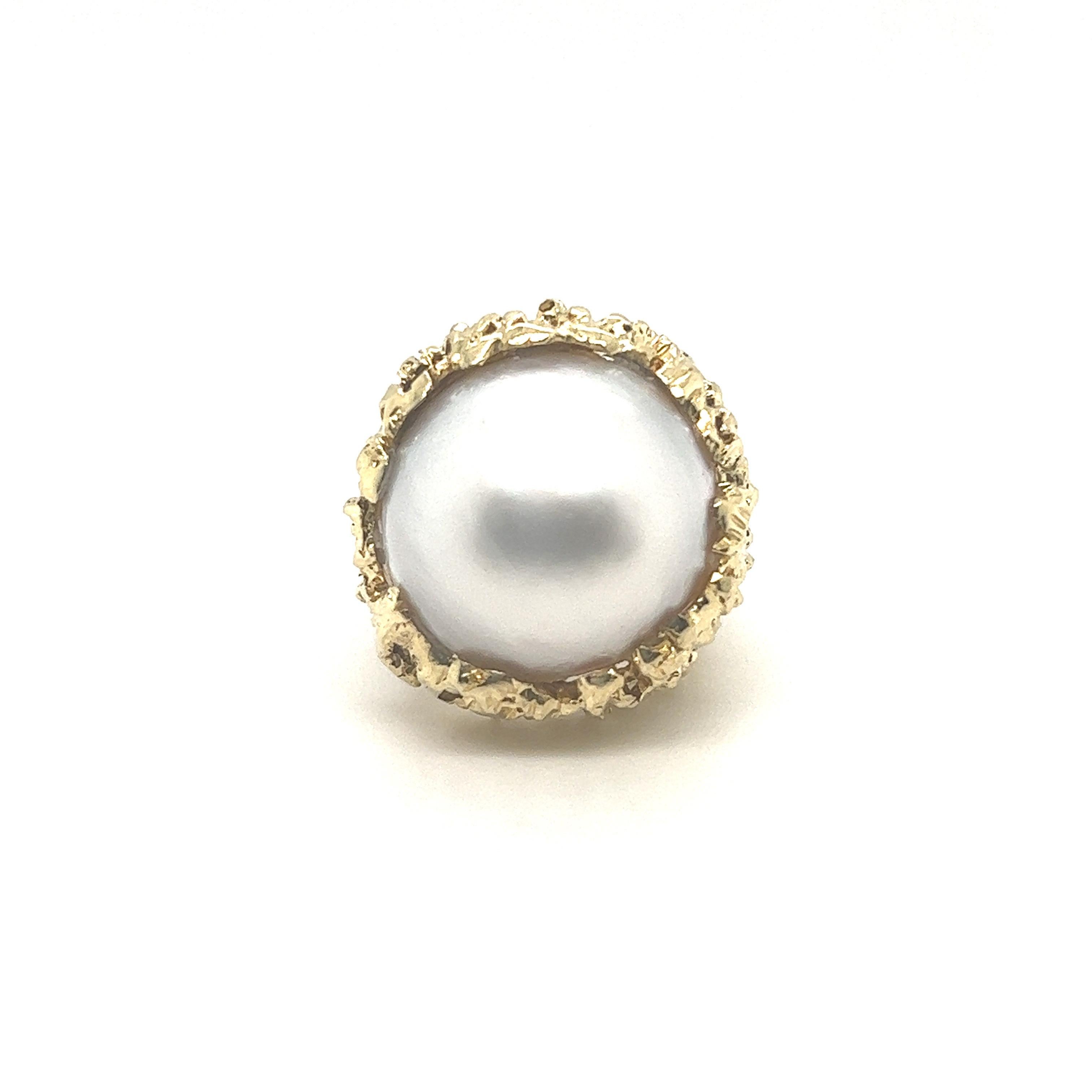 Glamorous and ladylike 14 karat yellow gold and mabe pearl cocktail ring from the 1970s. 
Crafted in 14 karat yellow gold, this eye-catching ring is set with a shiny mabe pearl of circa 1.8 cm / 0.7 inch diameter. The structured appearance of the