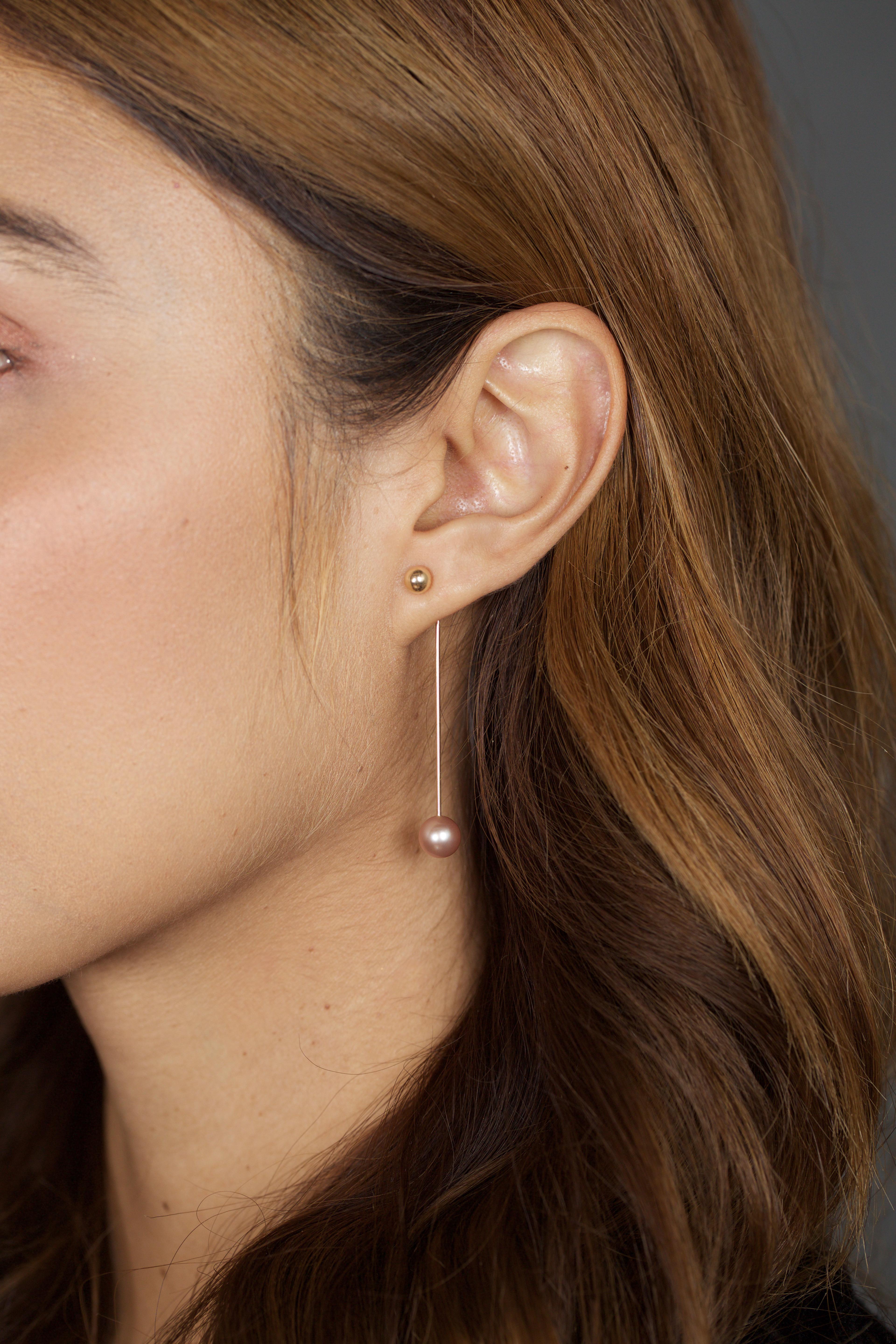 These earrings have a luminescent large pink pearl (can also be made with a white pearl)  which swings on a 14k yellow gold bar behind the earlobe.  It's paired with a classic gold ball stud, but you can change up the look anytime with a stud of