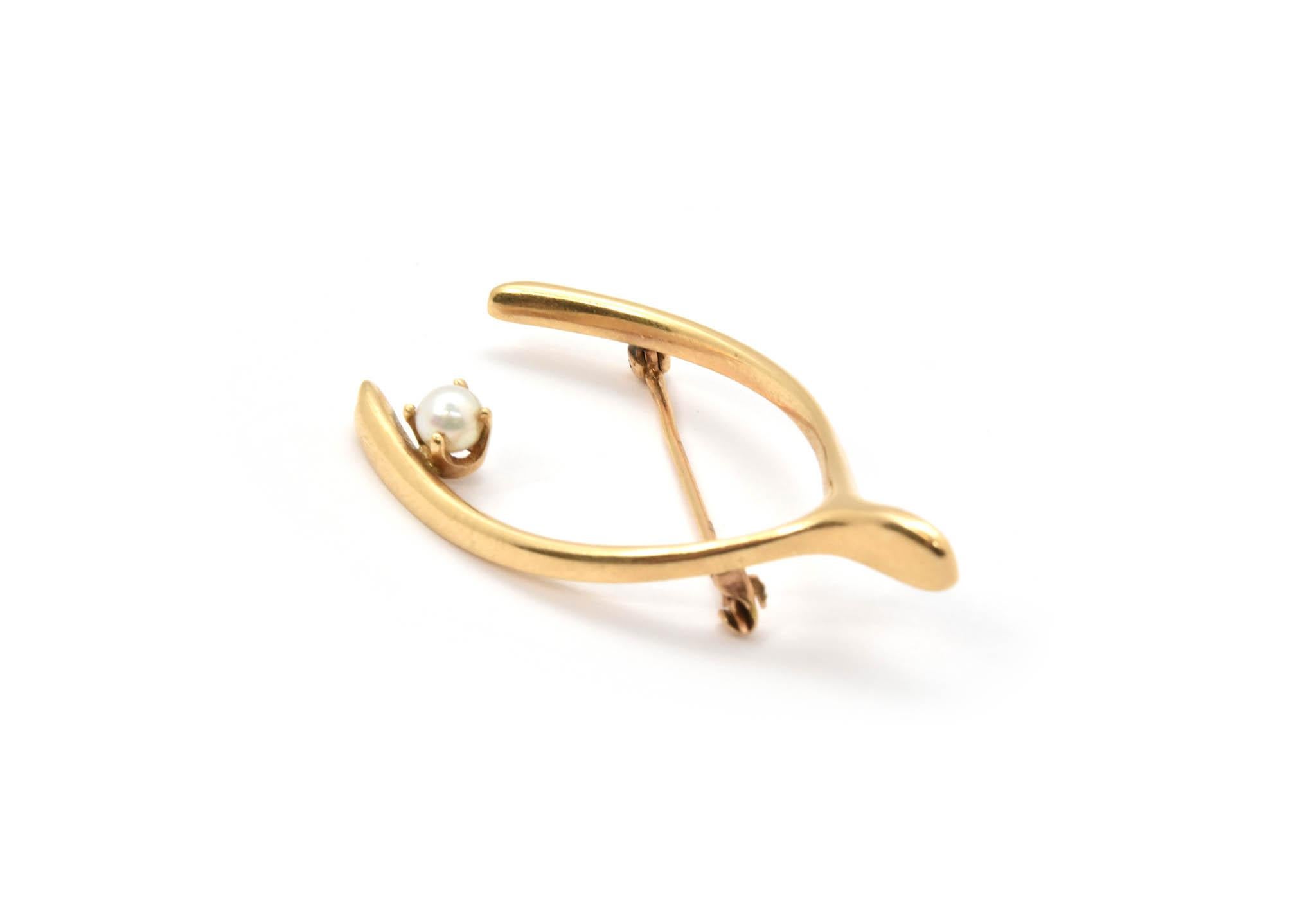 This brooch is made in 14k yellow gold with a single 4mm pearl in the shape of a wishbone. The brooch measures 42x24mm, and it weighs 5.56 grams.