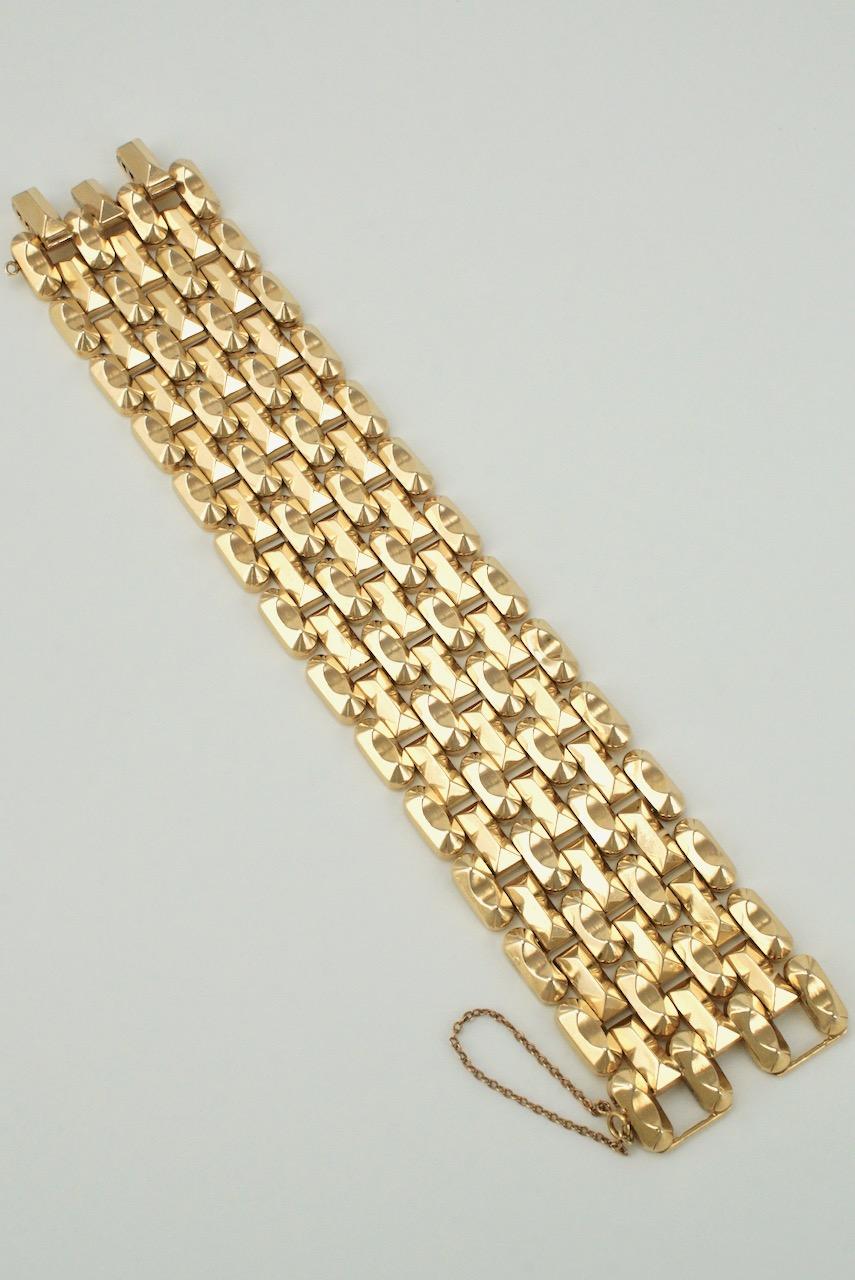 A 14k yellow gold wide Art Deco brick pattern link bracelet comprised of a staggered design of seven alternating rows of rectangular pyramid shaped links and saddle shaped links with a double integrated hinged clasp and a safety chain - the