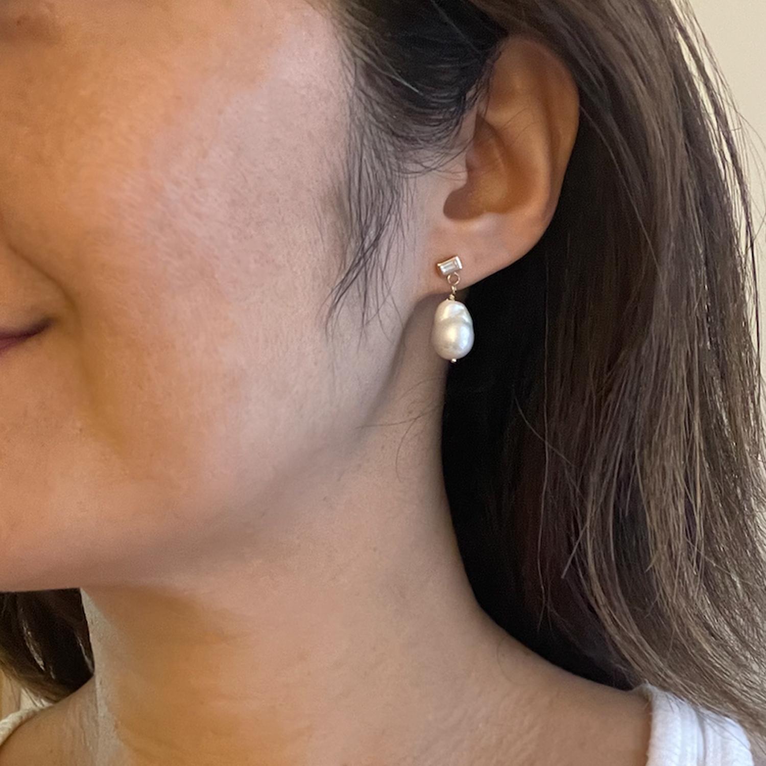 In these lustrous pearl drop earrings, a medium size gorgeous baroque pearl hangs from a VS1 quality baguette diamond stud earring. Pearls are the only gemstone that come from a living organism, and each baroque pearl shape will be slightly