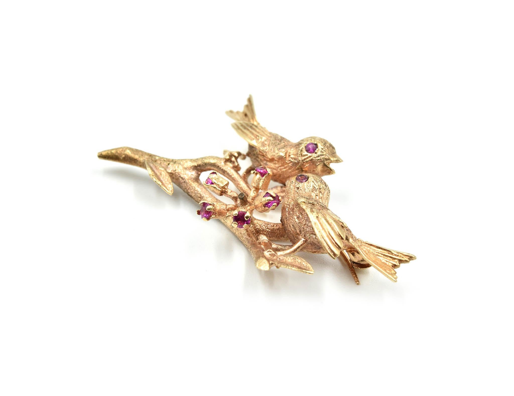 This antique pin illustrates two birds on a tree branch with ruby accents! The pin is made in 14k yellow gold with Victorian style designs made on it. The bird pin has no border and is held by the yellow gold tree branch. 5 rubies are prong set in